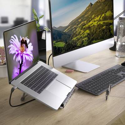 En bærbar computer med blomsterskærm står ved siden af en stor stationær skærm med bjerglandskab på et skrivebord med tastatur og mus.