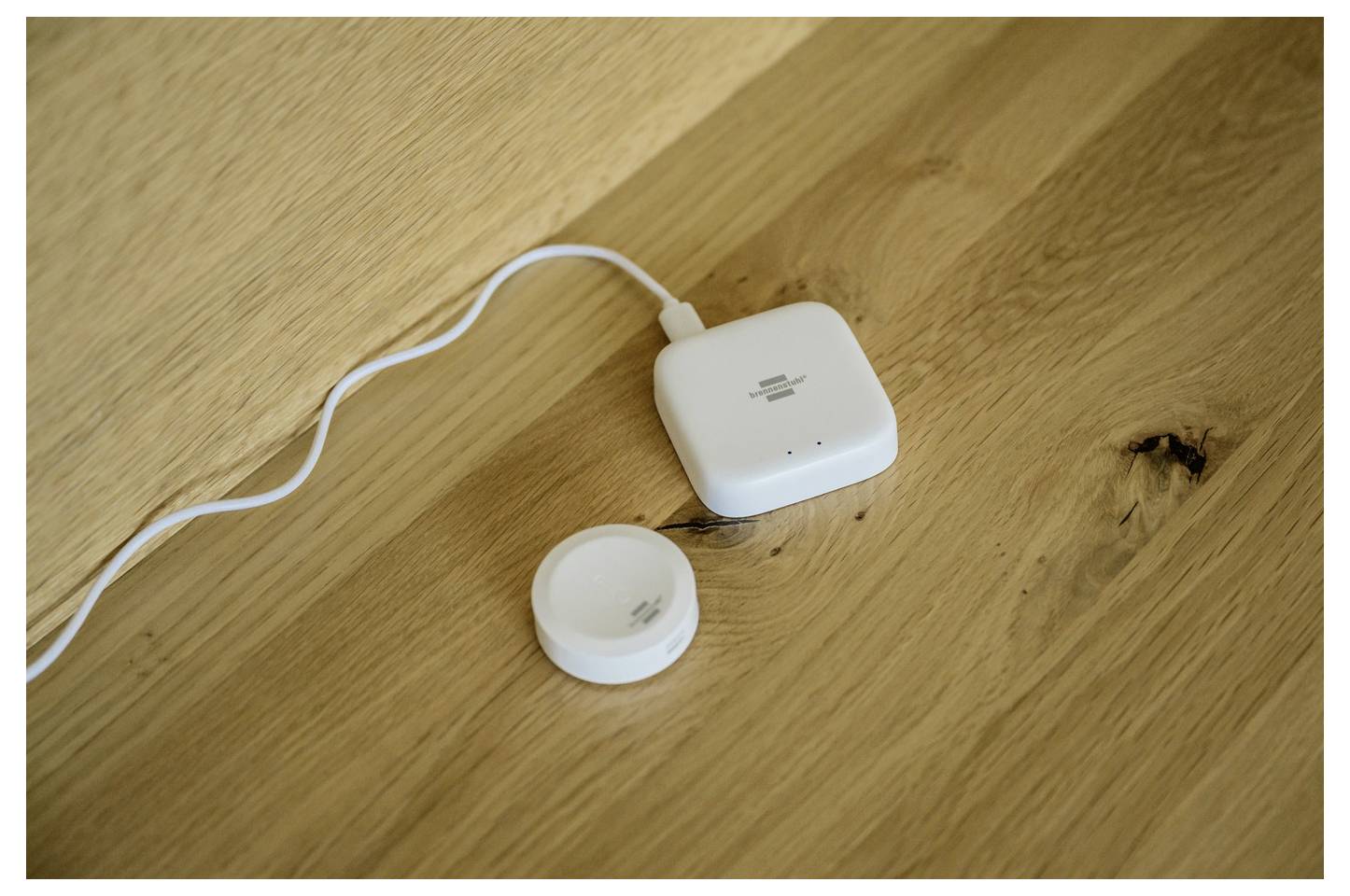 Hvid trådløs opladningspude med tilsluttet kabel og et lille rundt tilbehør, der hviler på et træbord.
