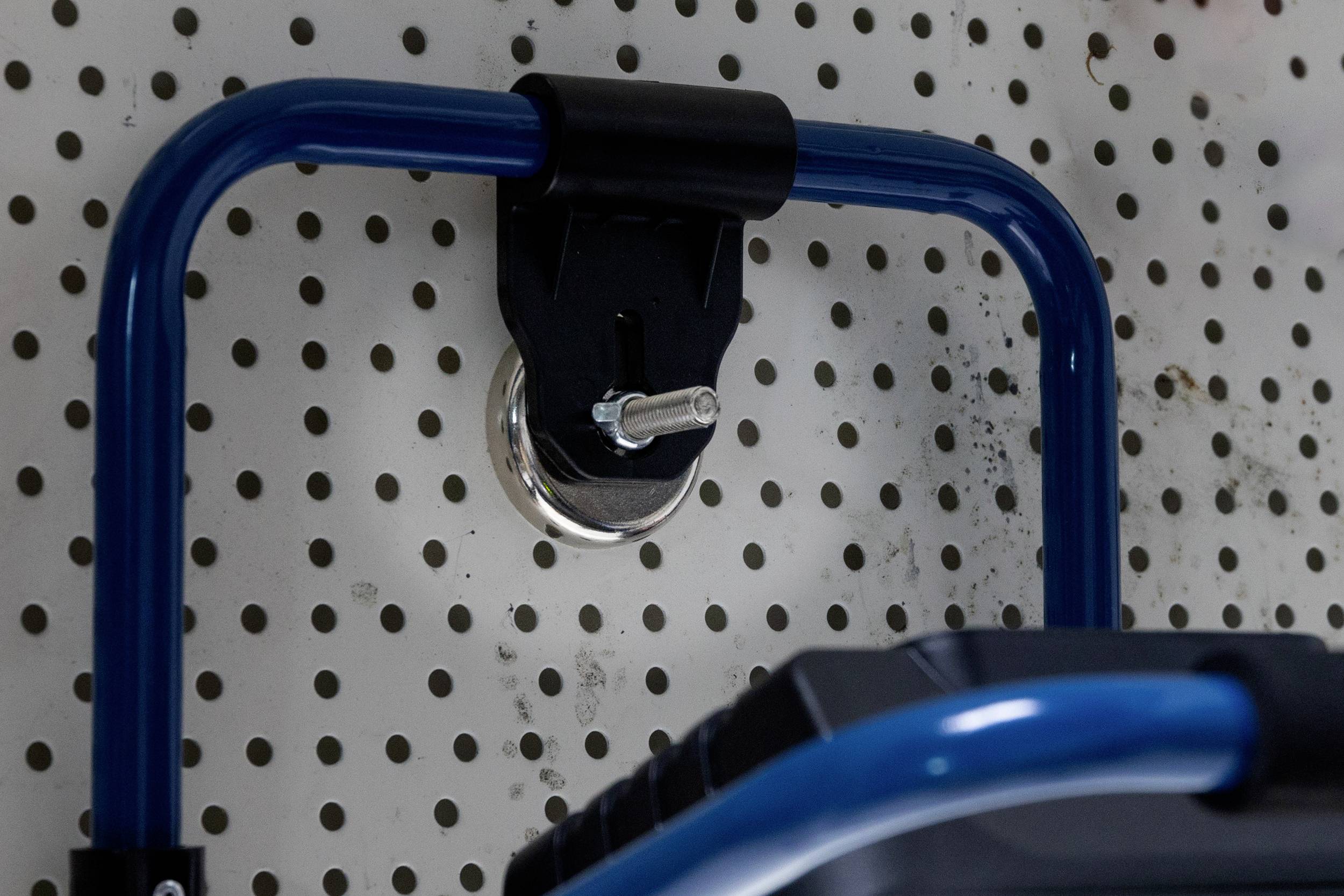 Værktøjsholder monteret på en hulplade, holder et blåt håndtag stabilt. Pladen viser rustpletter, hvilket indikerer brug.