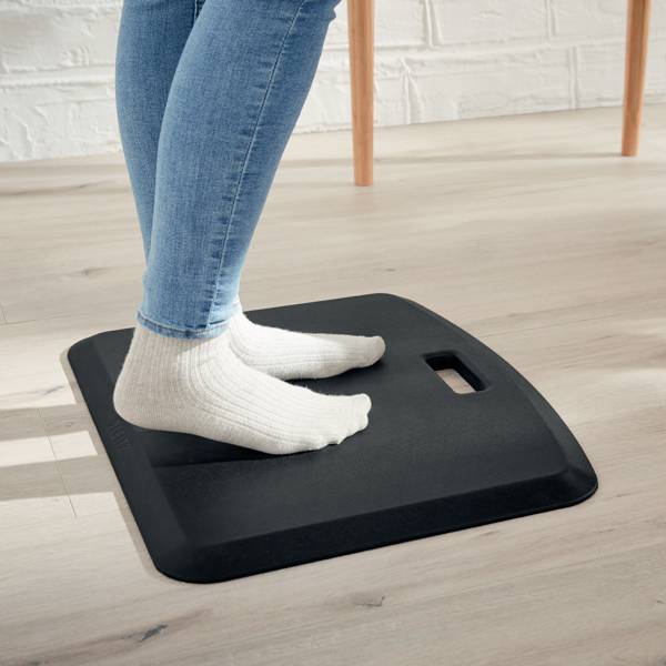 En person i blå jeans og hvide sokker står på et sort balancebræt på et trægulv.