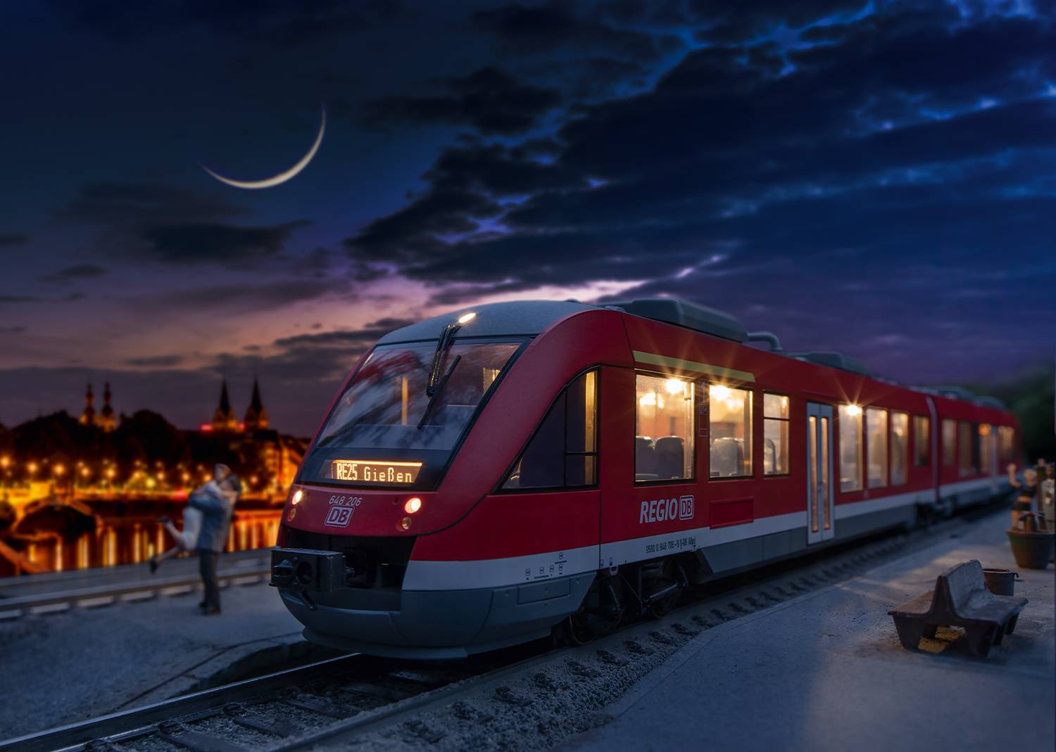 En rød lokaltog holder på perronen i aftenlyset, nedenunder en klar nattehimmel med en tynd månesikkel.