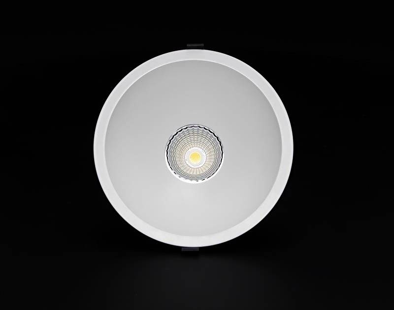 Rund loftslampe med metalramme, centreret i midten, udsender varmt lys, foran sort baggrund.