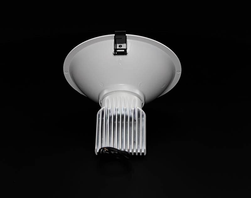 Rund, sølvfarvet loftslampe med køleribber og sort beslag, foran sort baggrund.