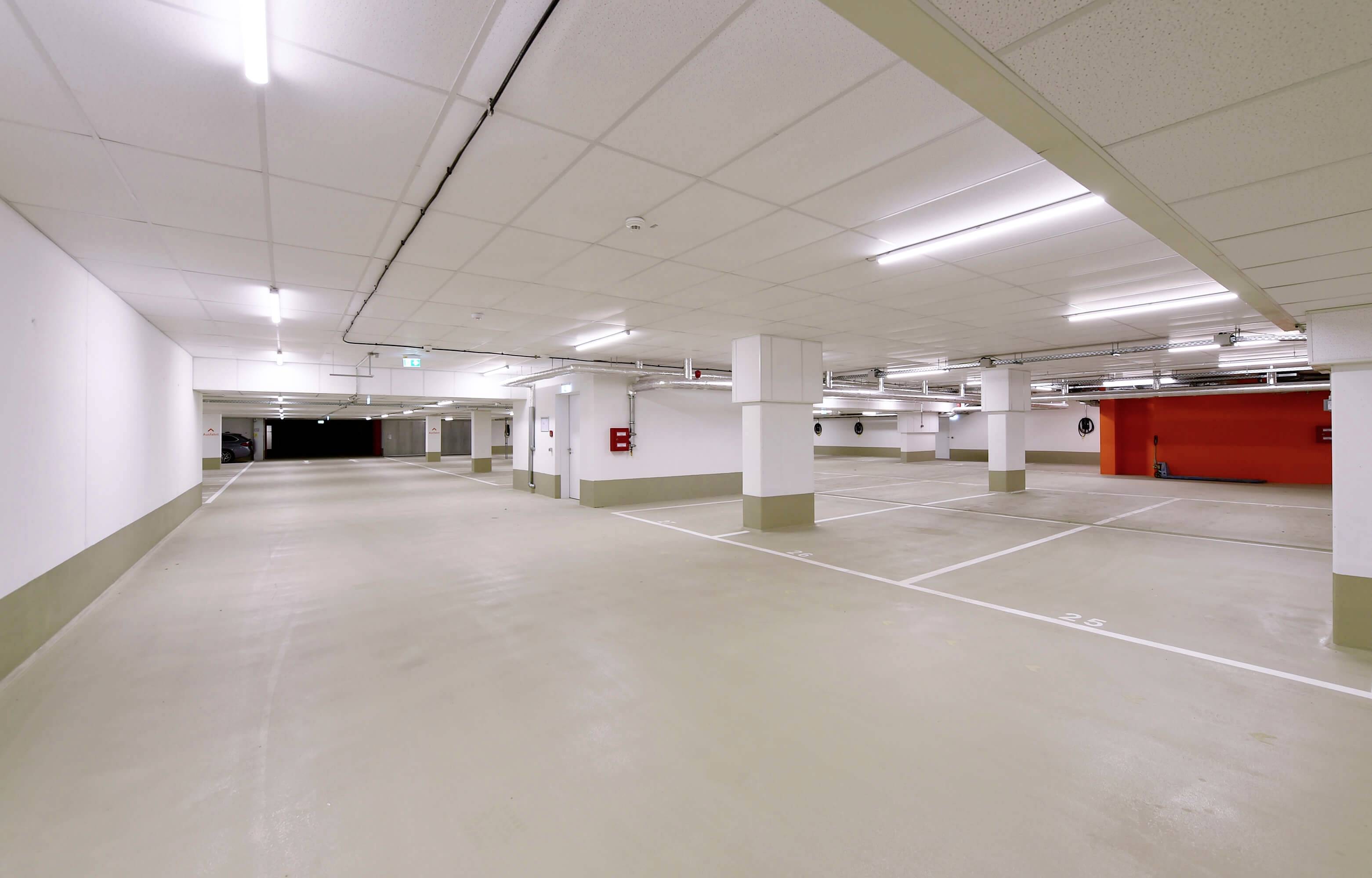 En tom, veloplyst parkeringskælder med hvide vægge og markeringer på gulvet. På væggen hænger der en brandslukkert.