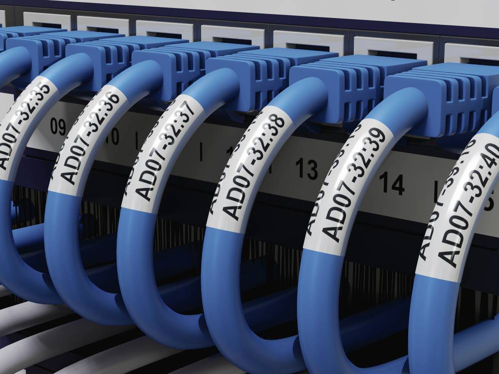 Netværksswitch med blå Ethernet-kabler, der er sat i nummererede porte. Kabler er mærket med 'AD07-32:36'-koder.