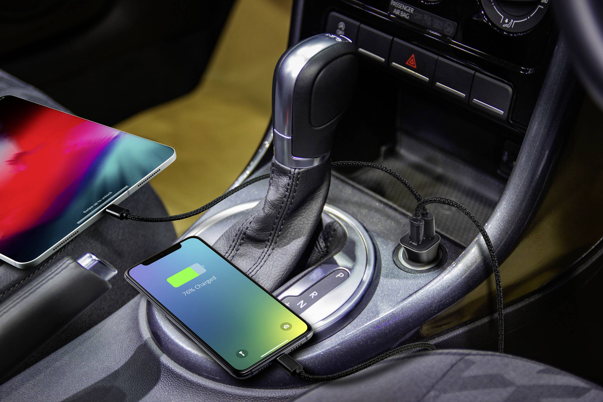 En smartphone og en tablet er tilsluttet og oplader i bilen; smartphonens display viser '100% opladet'.
