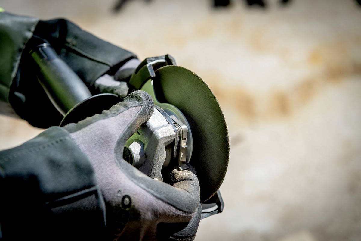 Nærbillede af hænder med beskyttelseshandsker, der holder en roterende slibeværktøj. Gnister flyver under metalbehandling.