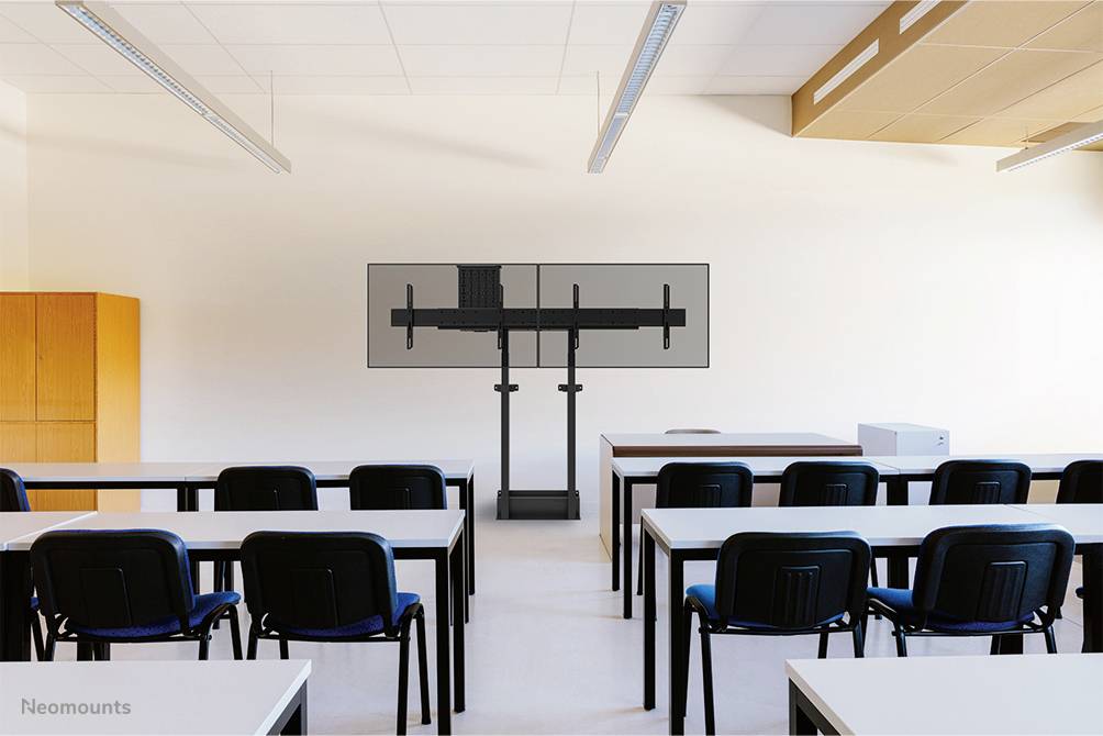 Et klasseværelse med flere skriveborde og stole, i baggrunden en tom skærmstander uden skærm, neutrale farver.