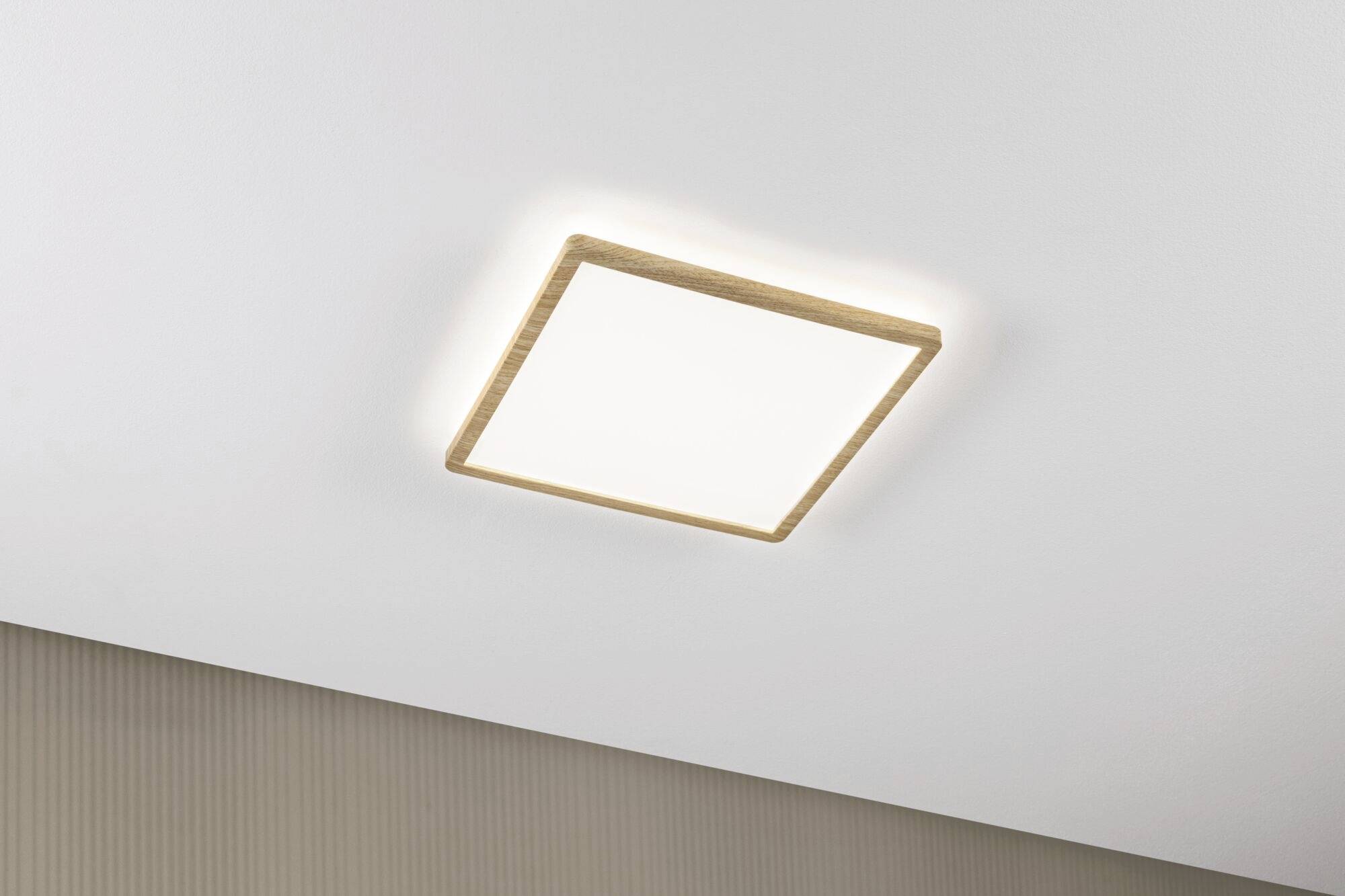 Firkantet loftlampe med træramme monteret på en hvid lofts flade. Blødtdæmpet lys oplyser rummet ensartet.