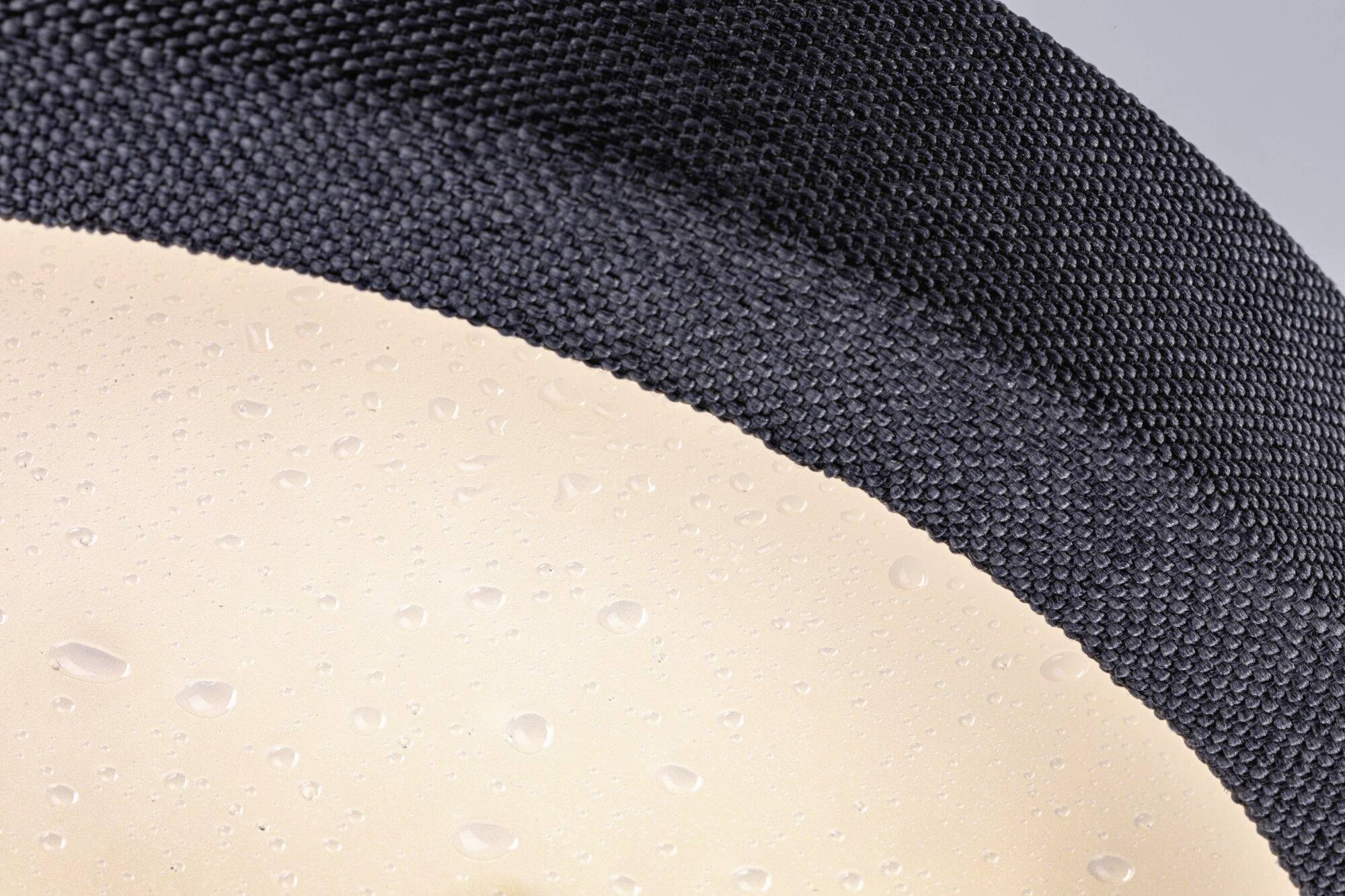 Nærbillede af en tekstiloverflade med sorte fibre og en underliggende beige lag med vanddråber.
