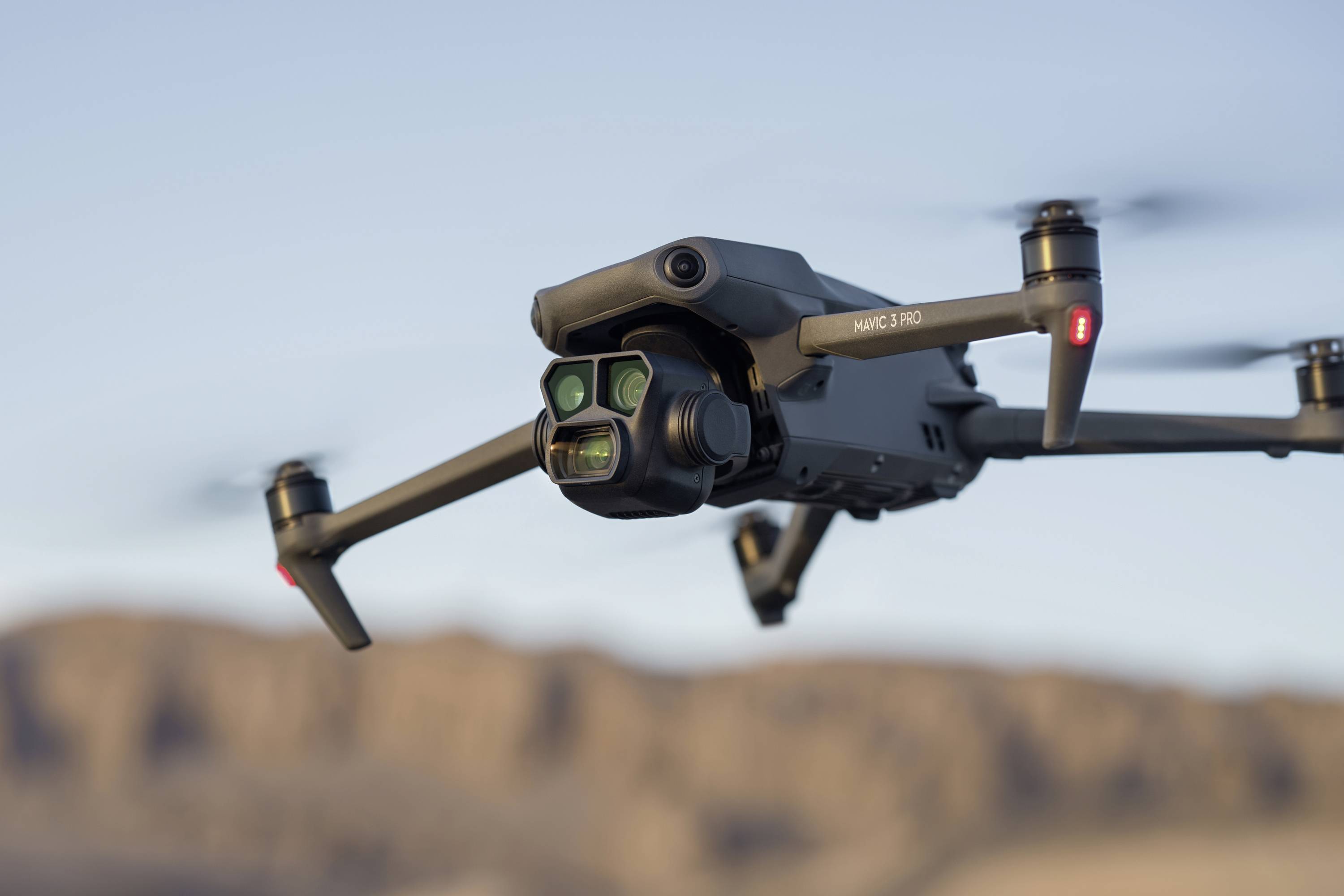 Nærbillede af en flyvende drone med fire propeller i et bjergområde. I baggrunden en sløret himmel og bjerge.