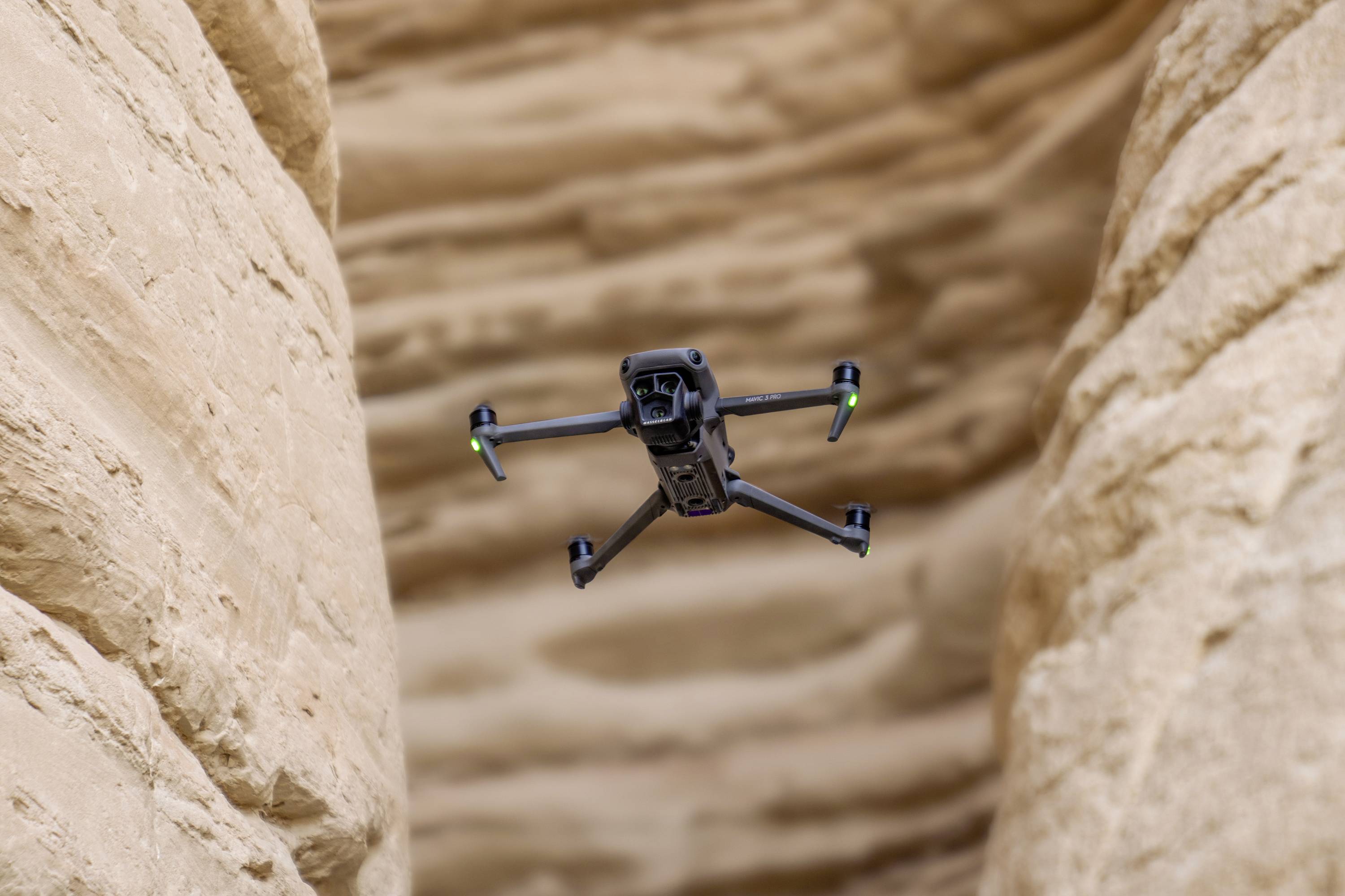 En drone flyver mellem to høje klipper i en slugt. Den ses forfra med grønne lys på vingerne.