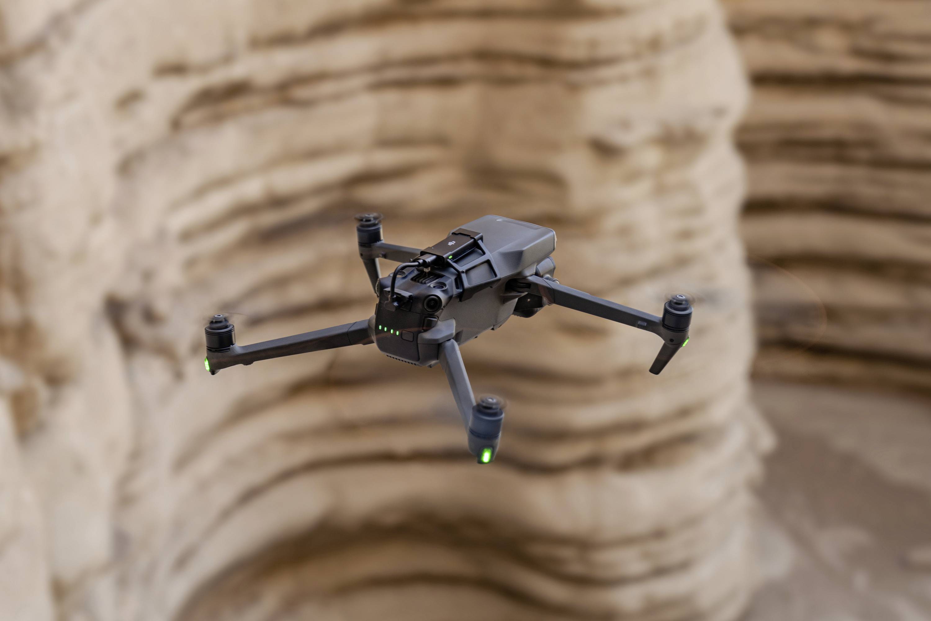 En sort drone svæver over en klippefyldt kløft med eroderede bjerglag i baggrunden.