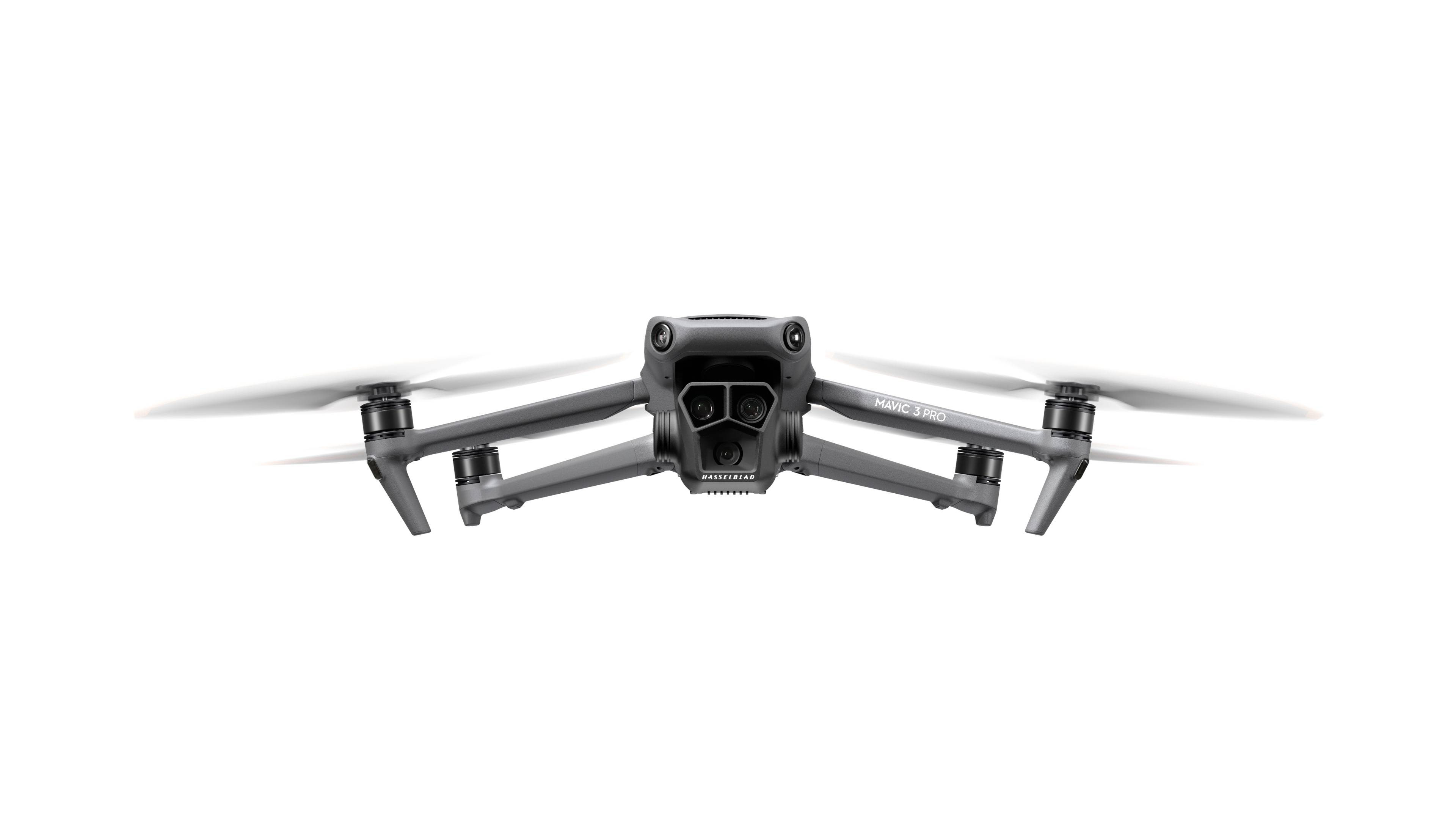 En grå drone med fire rotorer flyver frontalt mod en hvid baggrund.