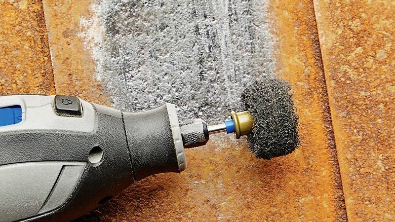 En roterende stålbørste på et elværktøj fjerner rust fra en metaloverflade. Metallet skifter fra brunt til sølvfarvet.