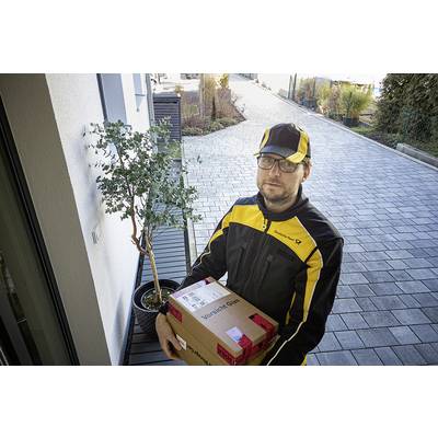 En udbringer i gul og sort uniform holder en pakke foran en hoveddør med en moderne indkørsel og et lille træ i en krukke.