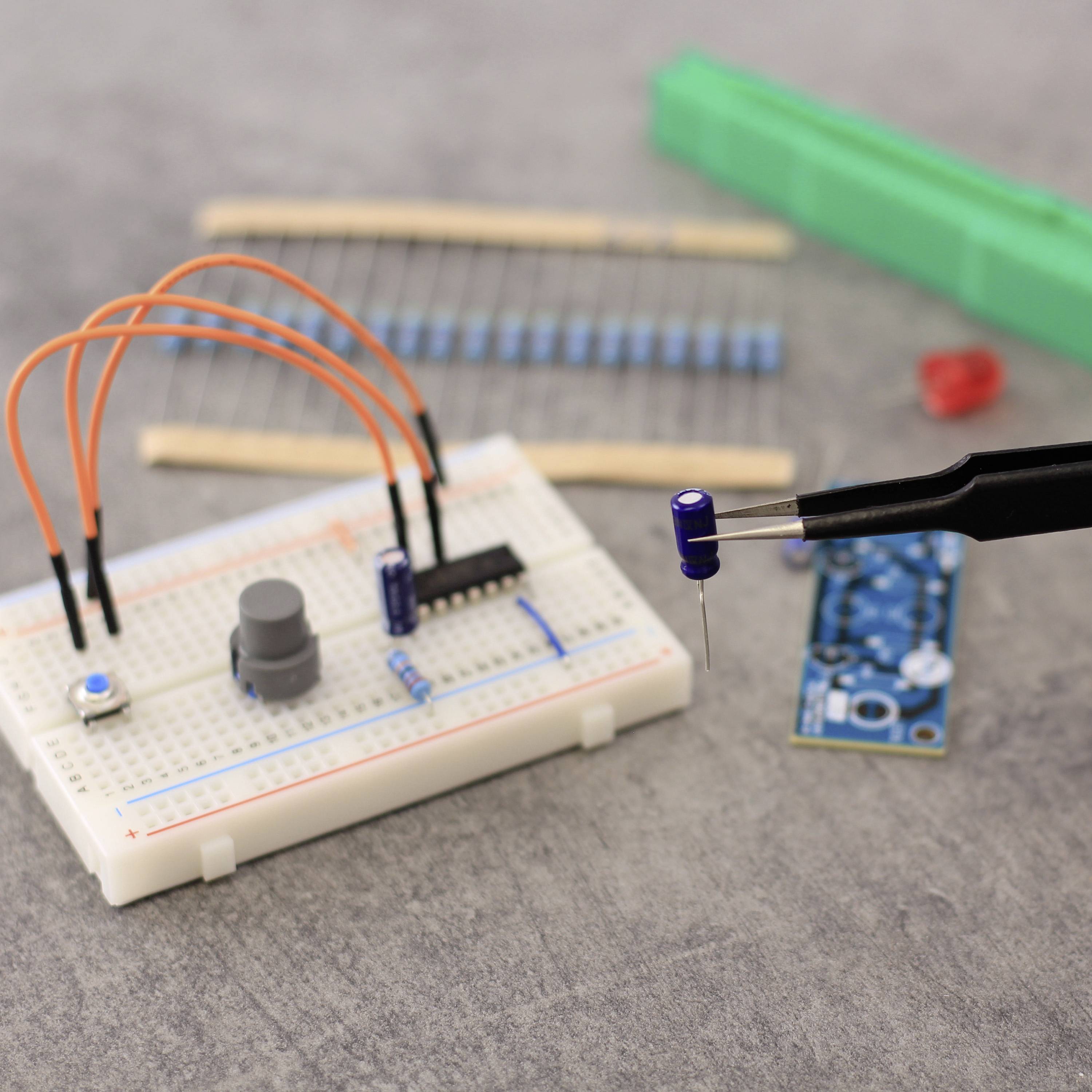 Elektronikopsætning med breadboard, modstande, kondensator og sensor. Loddekolbe med blå spids i nærbillede.