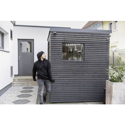 En person i mørk tøj trækker et moderne, lille havehus hen over en grusvej. I baggrunden ses en lys bygning.