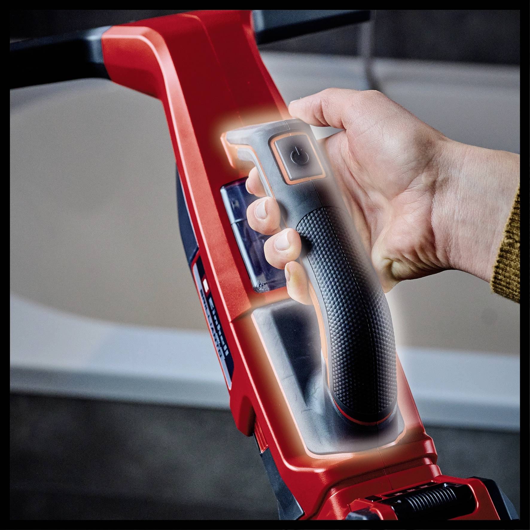 En hånd holder grebet på en rød elværktøjsmaskine, formentlig en borehammer. Fokus er på det ergonomiske design af grebet.