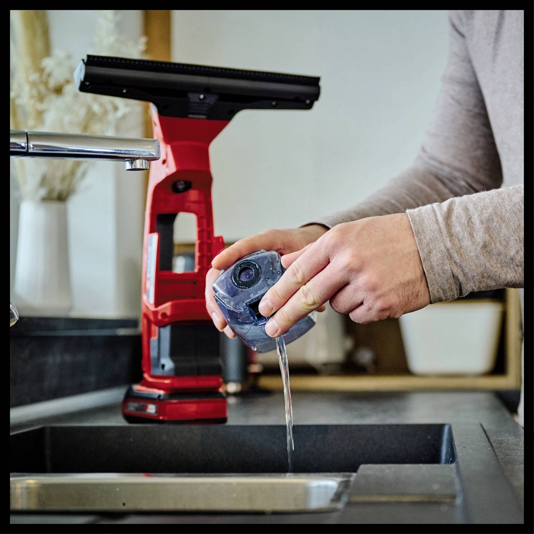 En person fylder vand på en vandtank foran en vandhane. I baggrunden ses en vinduesrenser.