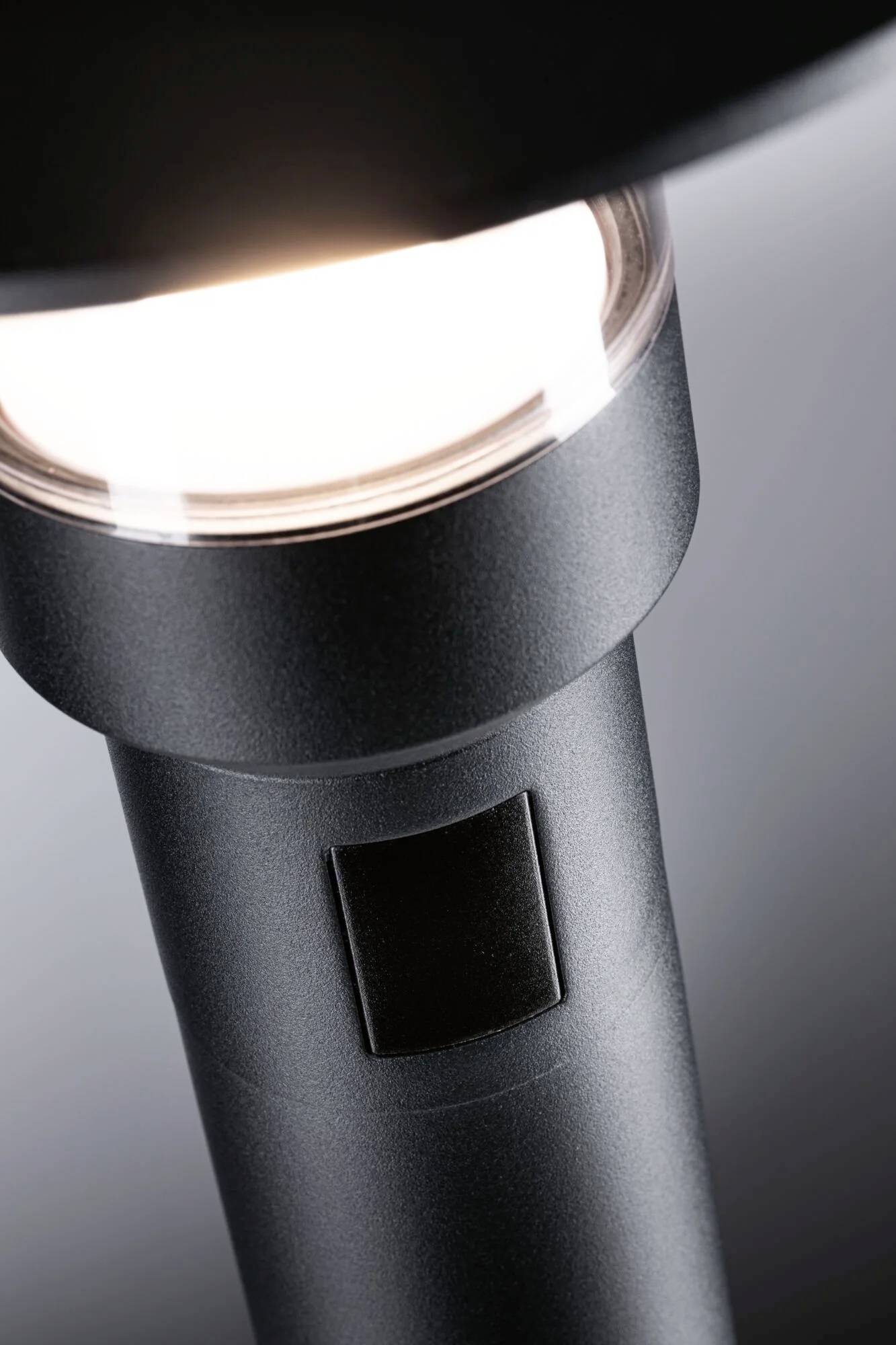 En moderne standerlampe i nærbillede, der udsender et blødt lys. Lampen har en enkel, sort metalramme.