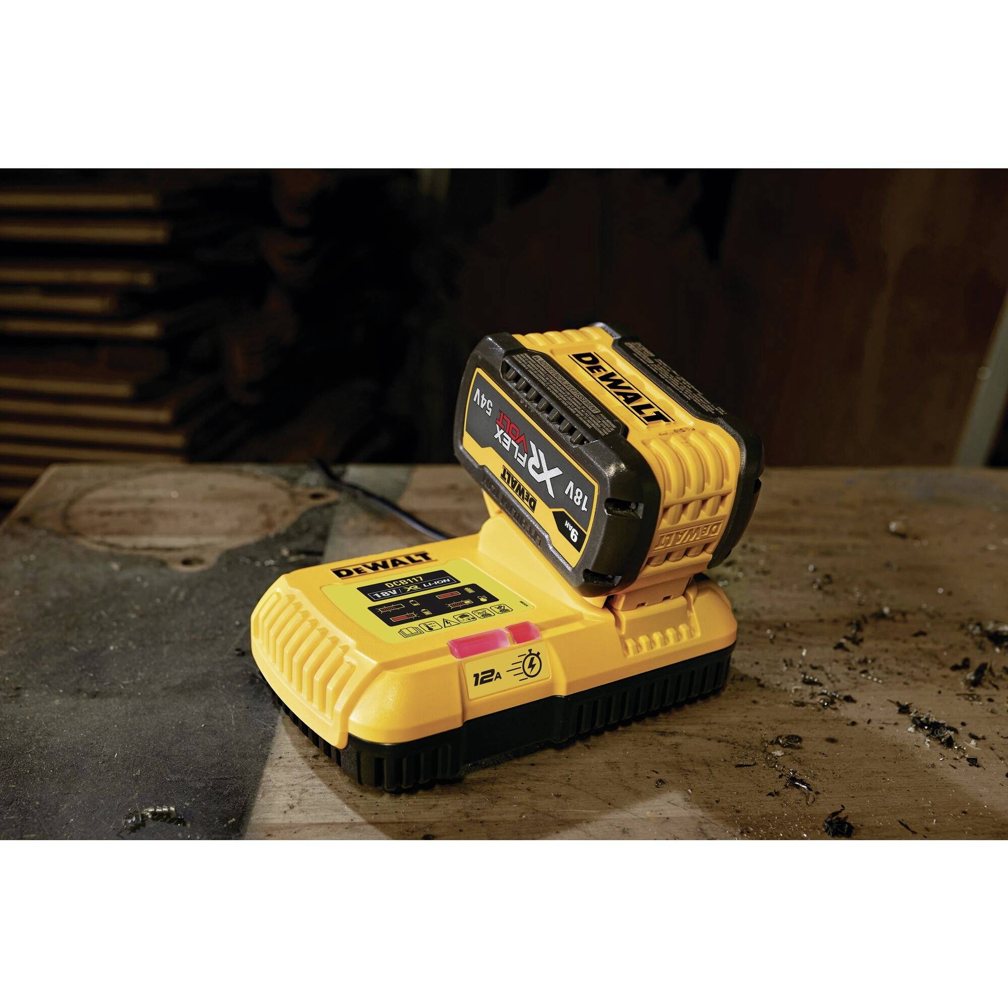 En gul batteri oplader på en passende ladestander på en arbejdsbænk. I baggrunden ses træstykker.