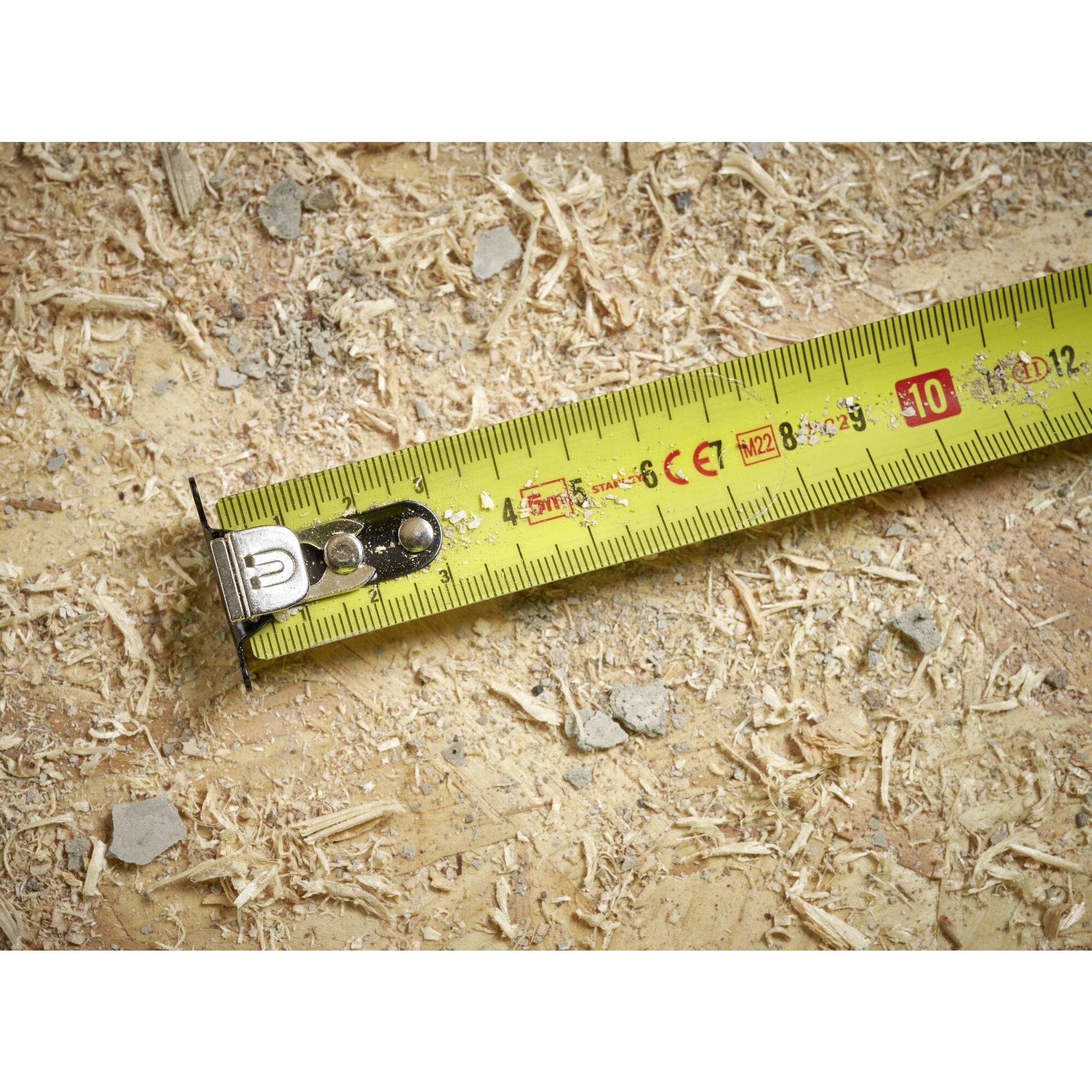 Nærbillede af et gult målebånd på en træoverflade med savspåner, der viser en længde på omkring 9 centimeter.