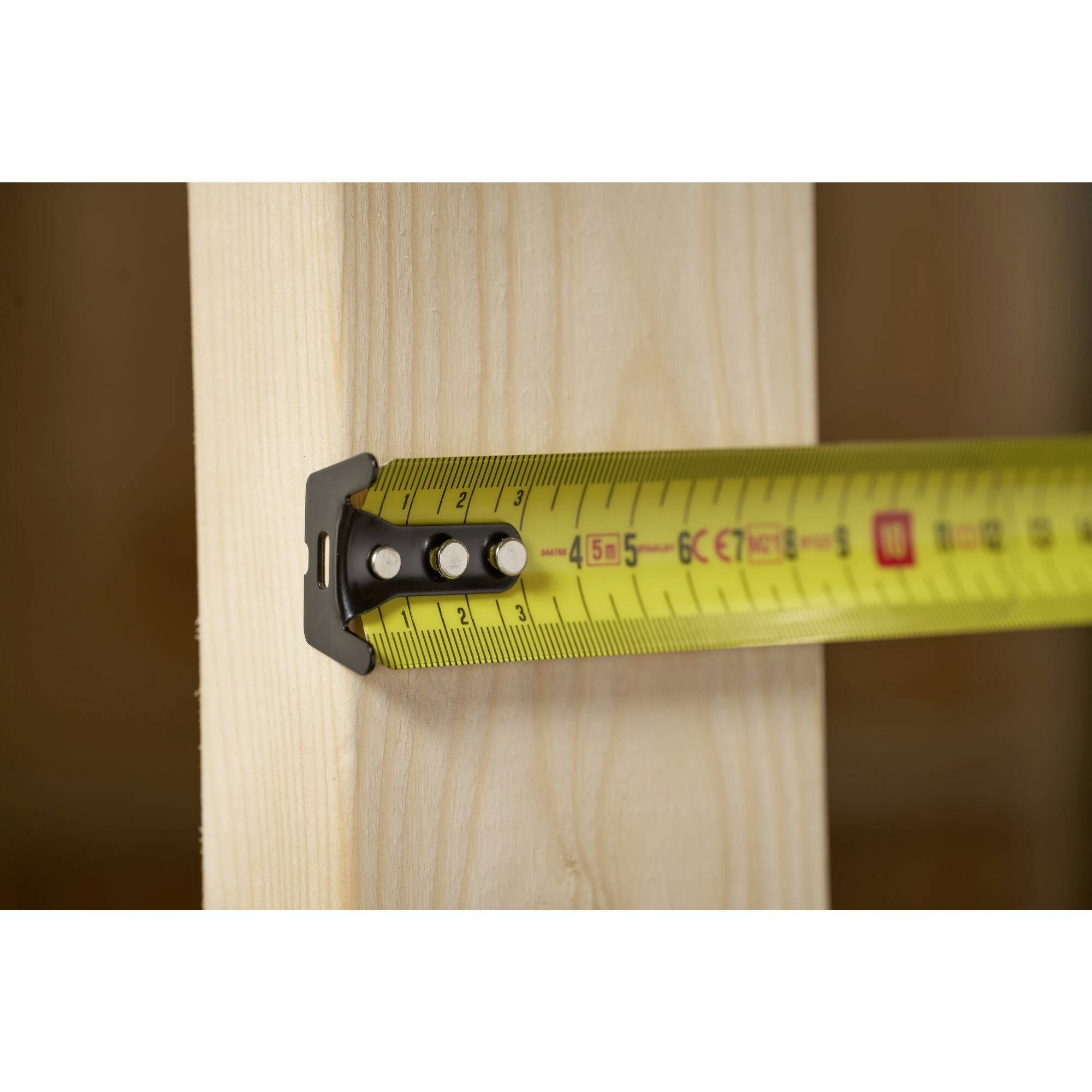 Et gult målebånd måler bredden af et stykke træ til omkring 5,5 centimeter.