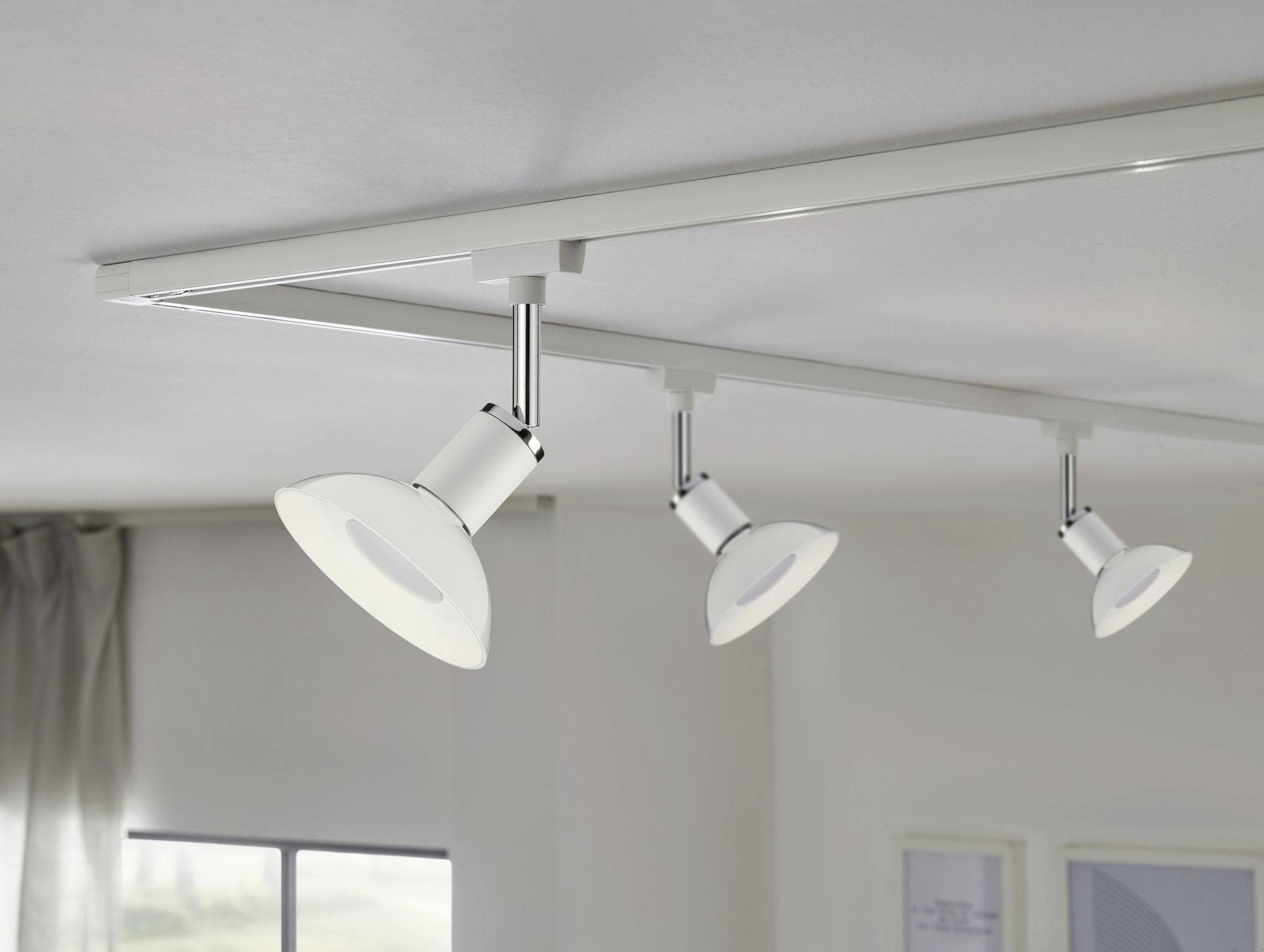 Tre hvide loftslamper monteret på en skinne i rummet. Klart dagslys fra venstre side.