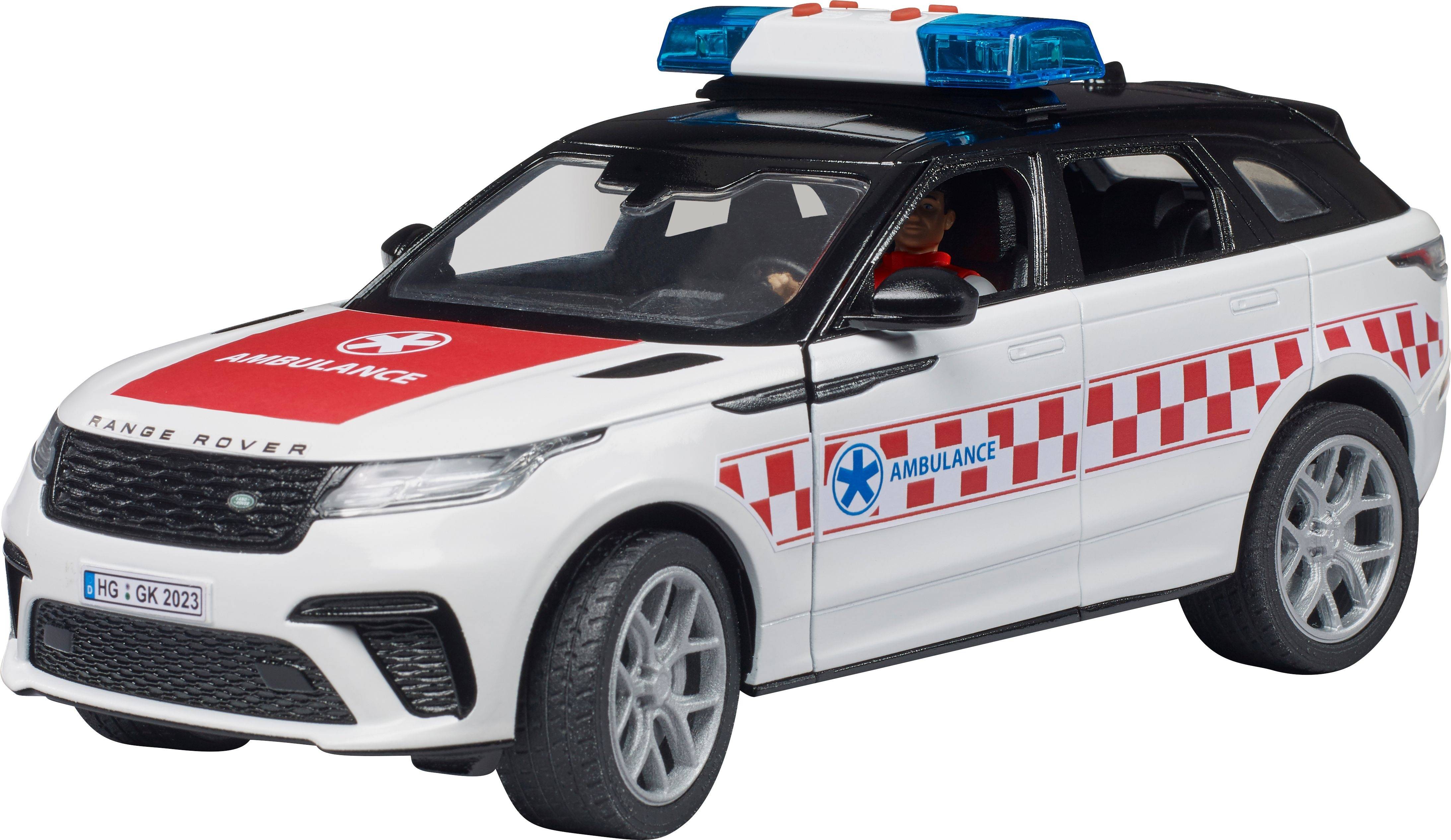En hvid redningskøretøj med røde firkanter og ordet 'Ambulance' på motorhjelmen. En mand sidder bag rattet.
