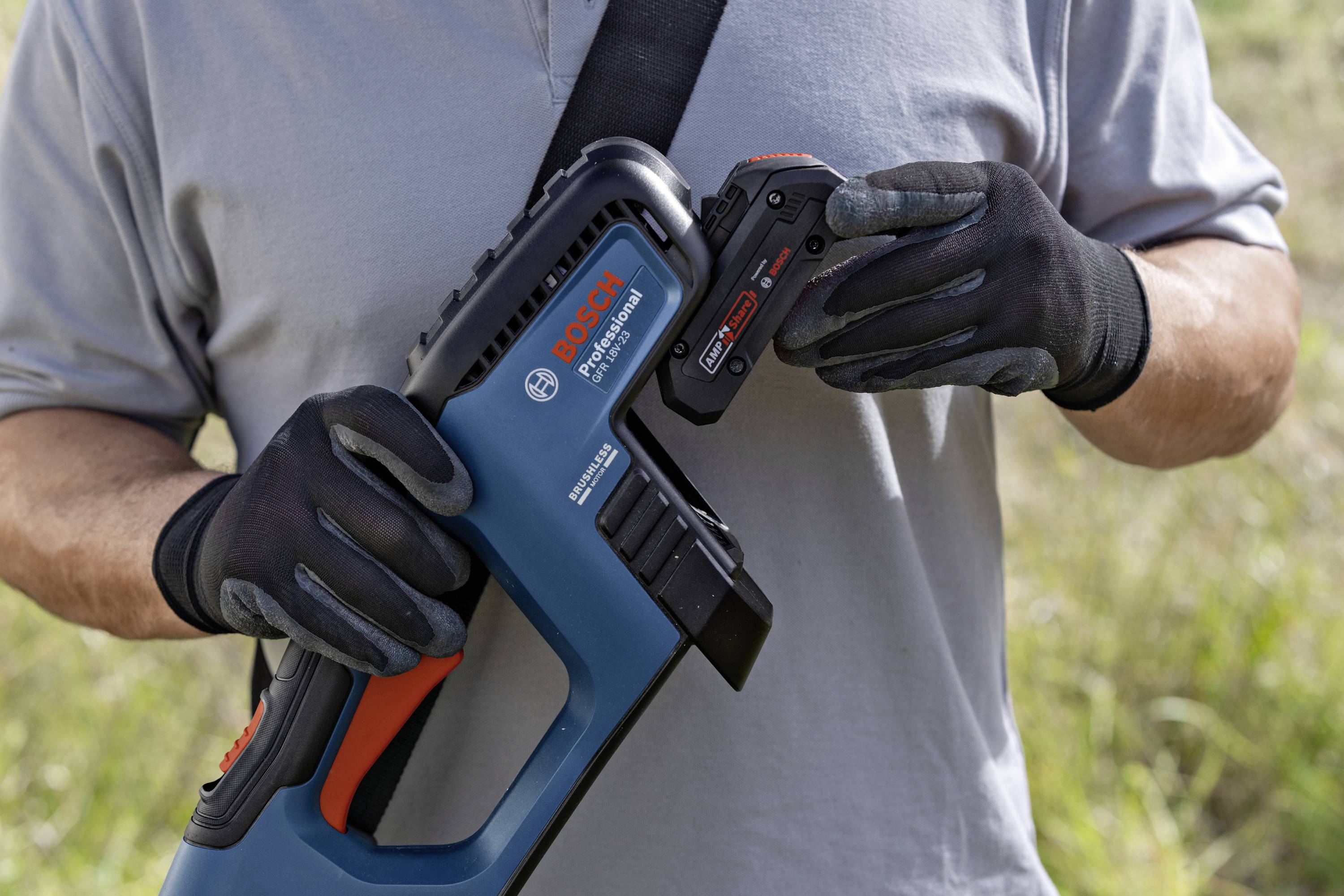 Mand i grå t-shirt og sorte handsker holder en Bosch akku-havesaks og et batteri udendørs.