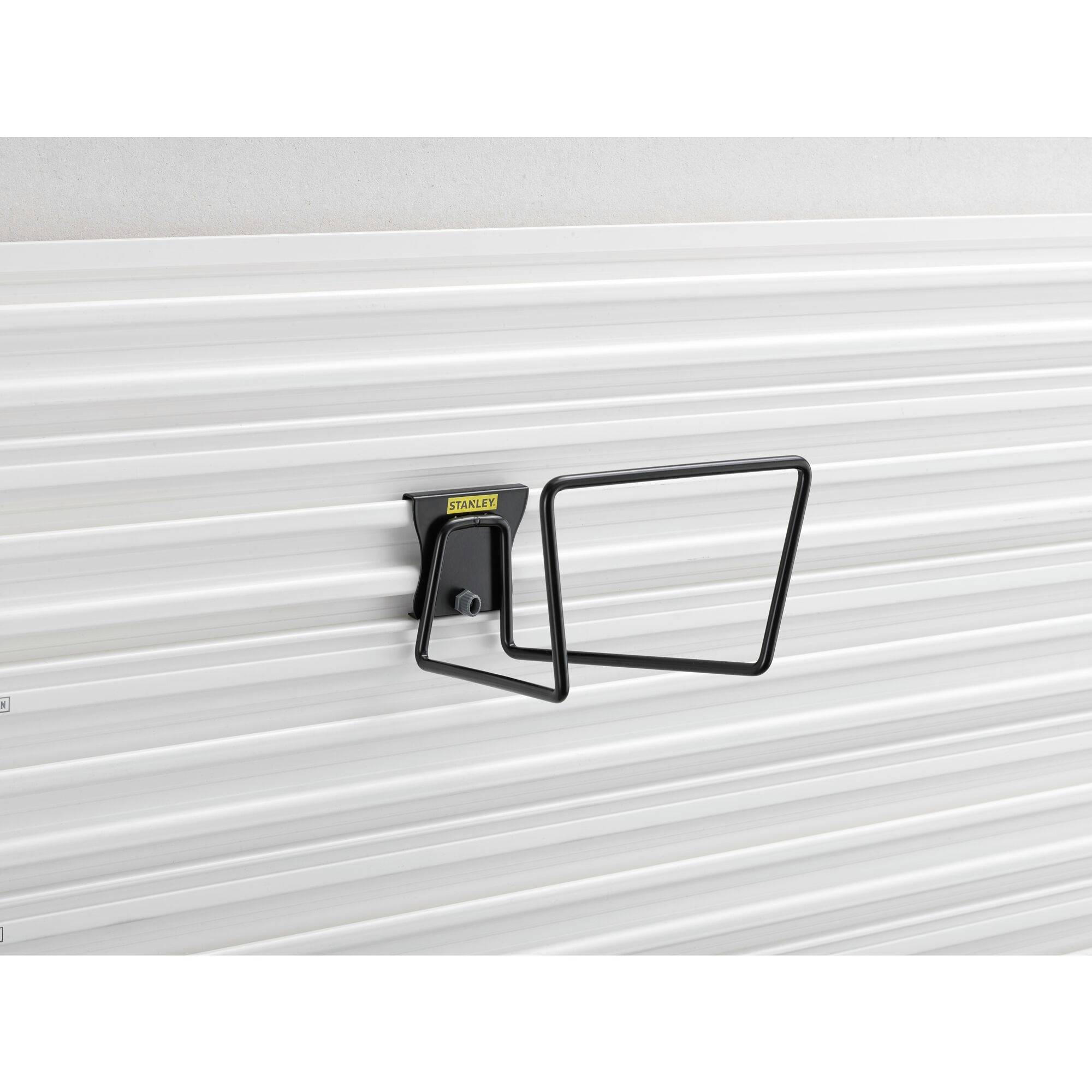 En sort, rektangulær metalkrog er monteret på en struktureret, lysegrå væg, egnet til at holde slanger.
