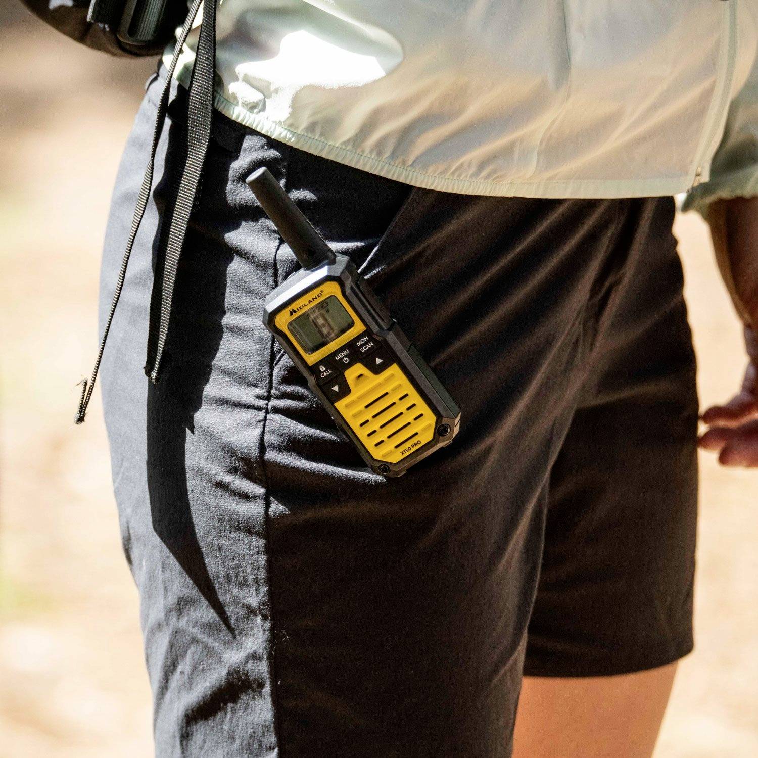 En person bærer en gul walkie-talkie ved bæltet, mens vedkommende vandrer i naturen.