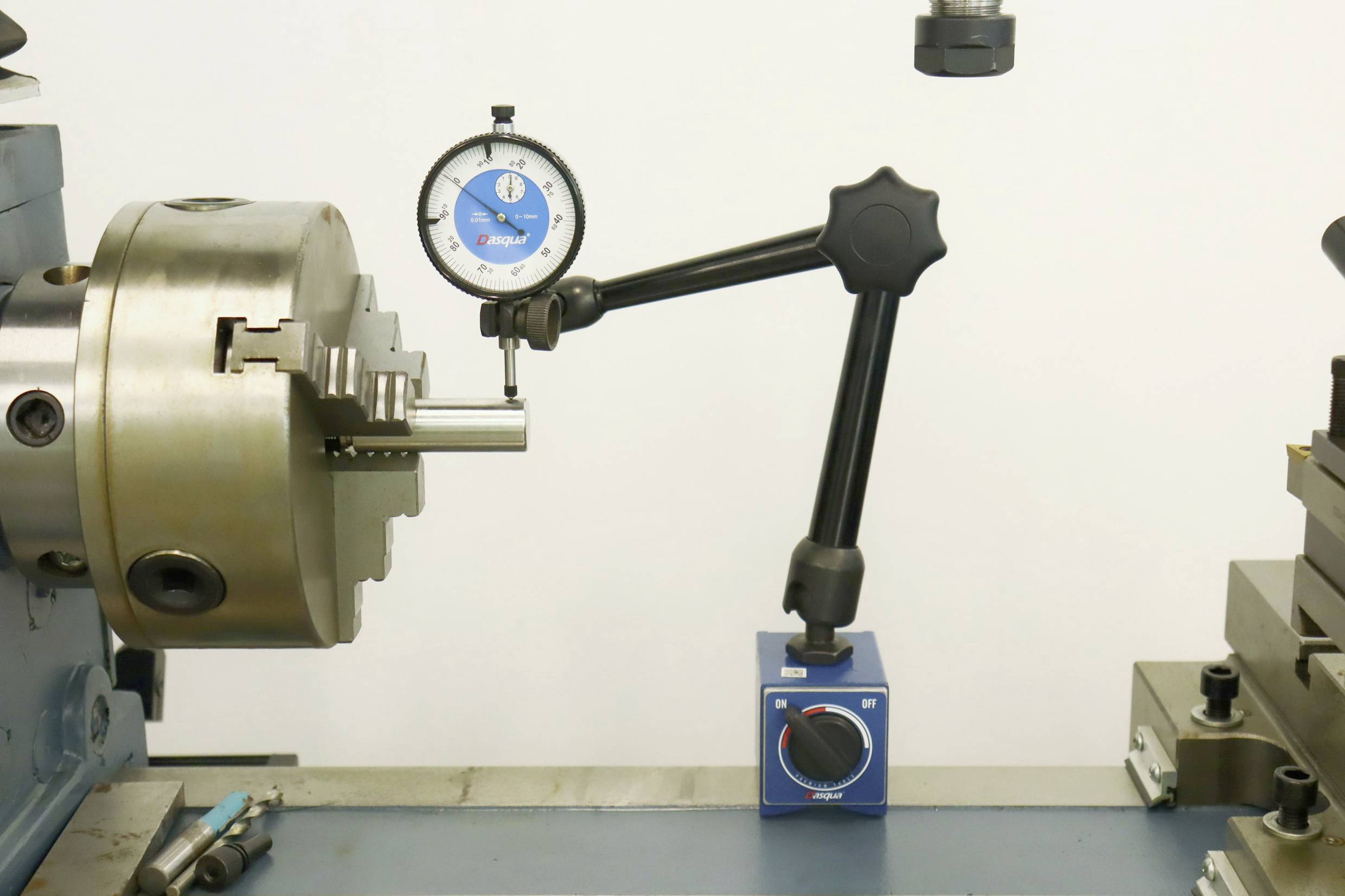 Et måleapparat med viser og skala måler rundheden af en metalcylinder, der er spændt fast i en drejebænk.