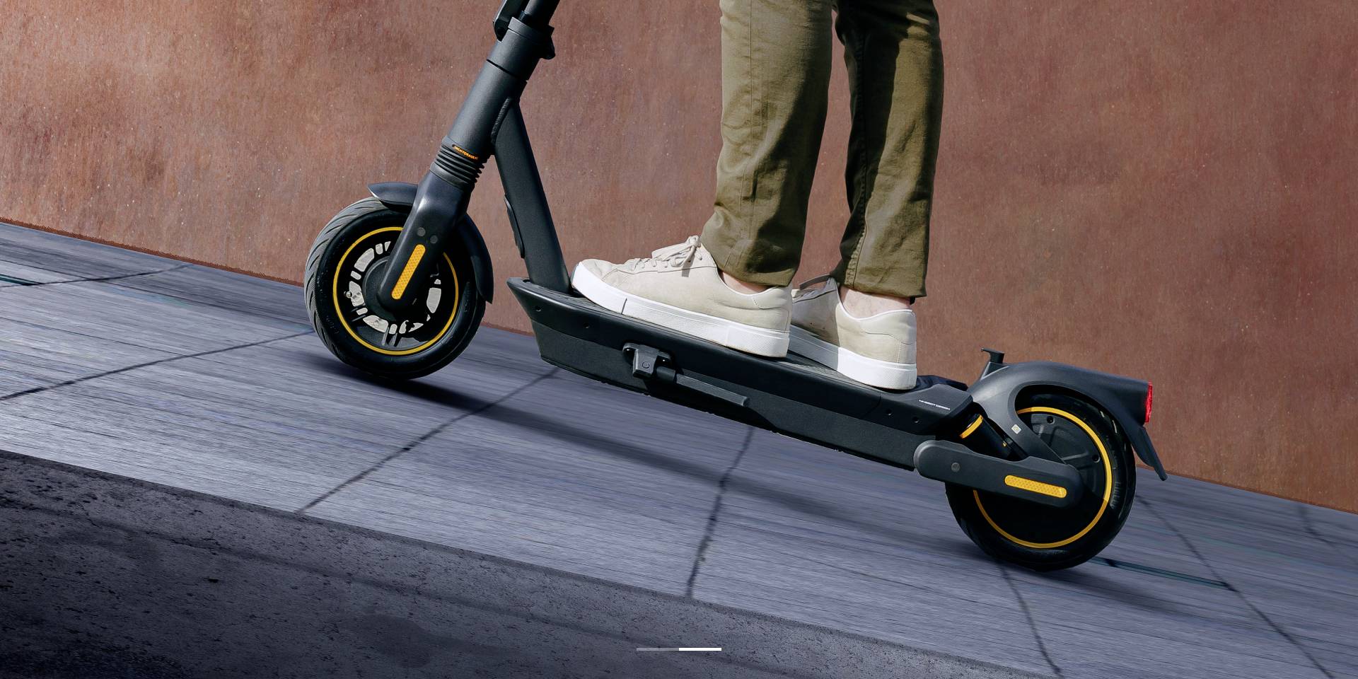 En person kører en sort elscooter på et fortov med grå fliser.