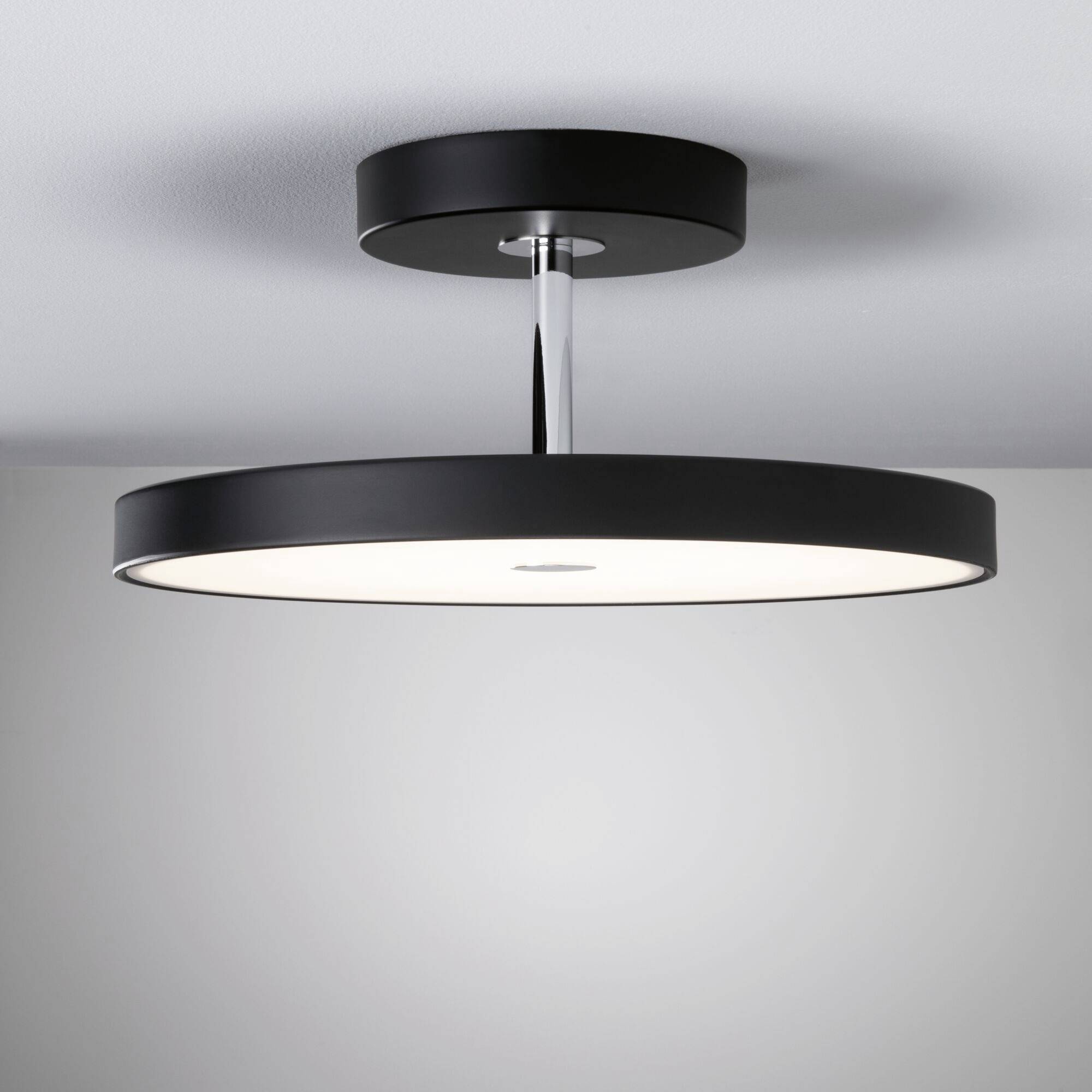 Sort, rund loftslampe med moderne design, hænger ned fra loftet og skaber ensartet, diffust lys i rummet.