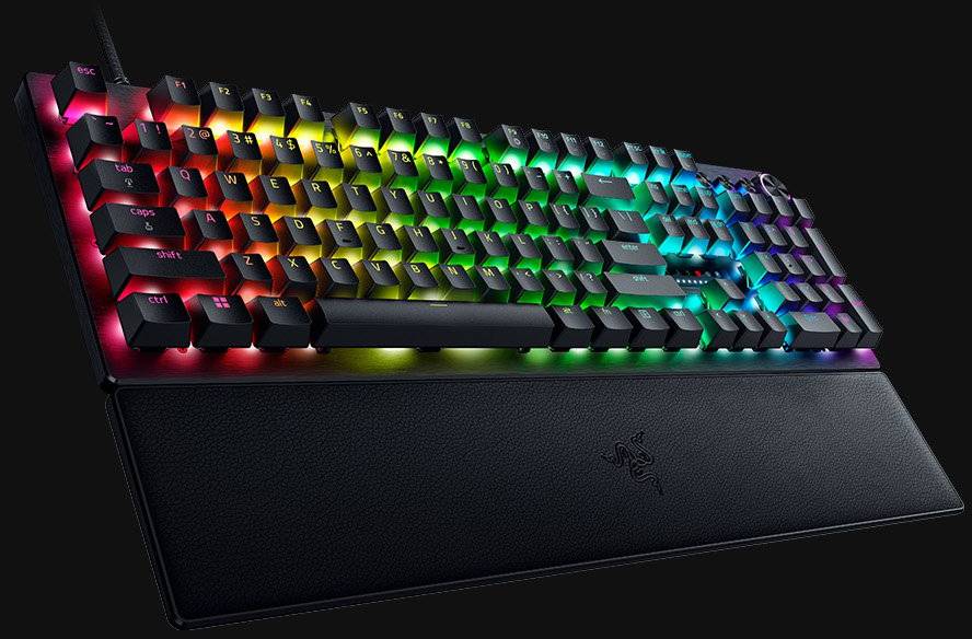 Mekanisk tastatur med RGB-belysning på sort baggrund. Tasterne lyser i forskellige farver og viser levende mønstre.
