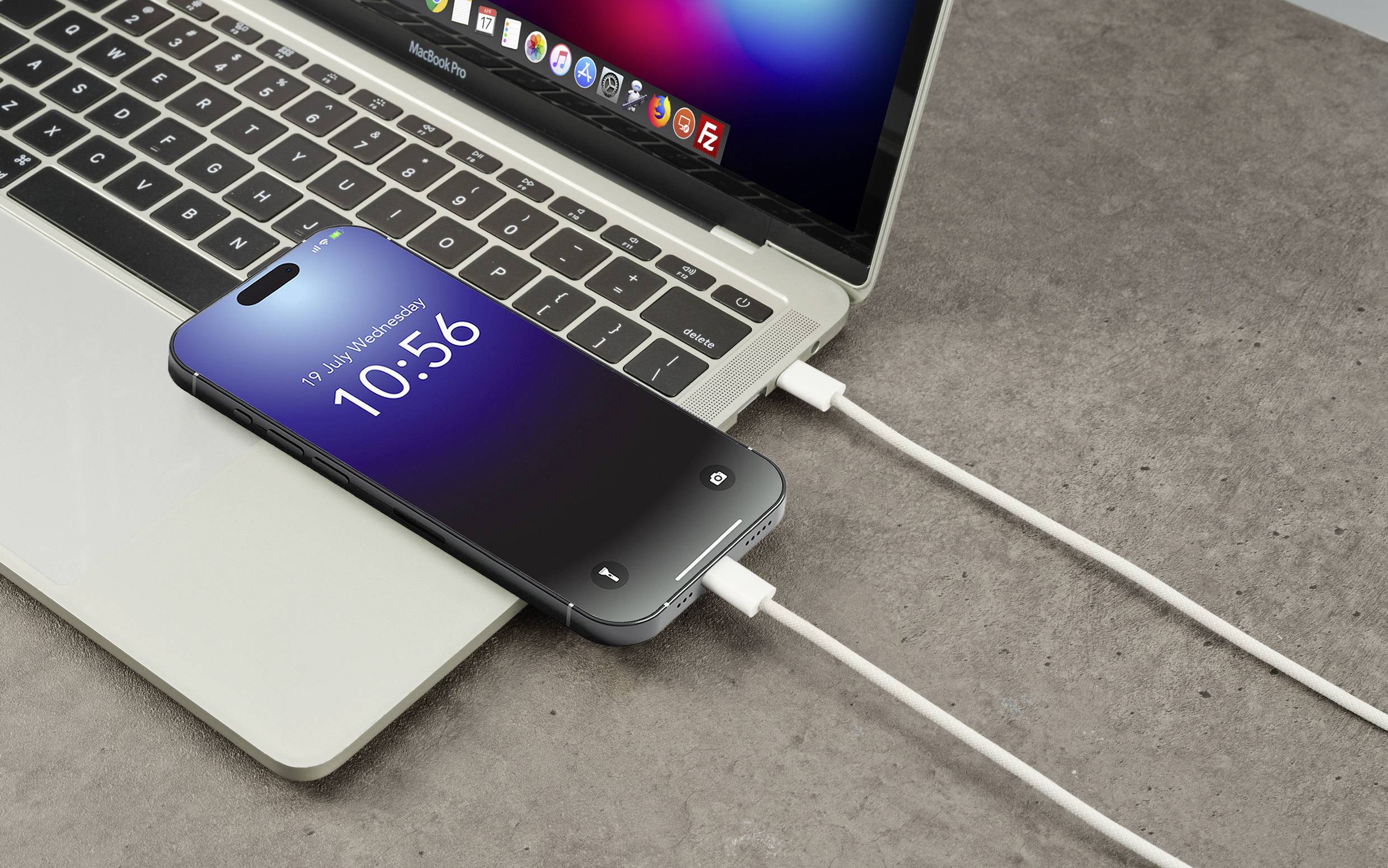 En smartphone oplades via et kabel, der er tilsluttet en bærbar computer. På smartphonens skærm vises klokken '10:56'.