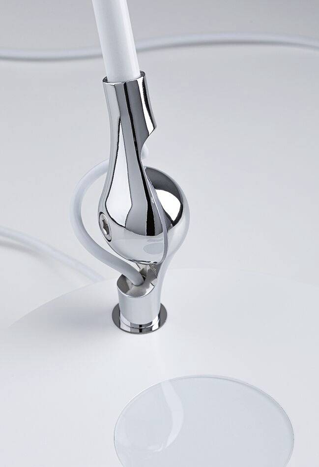 En moderne, blank bordlampe i metal med svungen hals og rund base på en hvid baggrund. Ledningen er synlig.