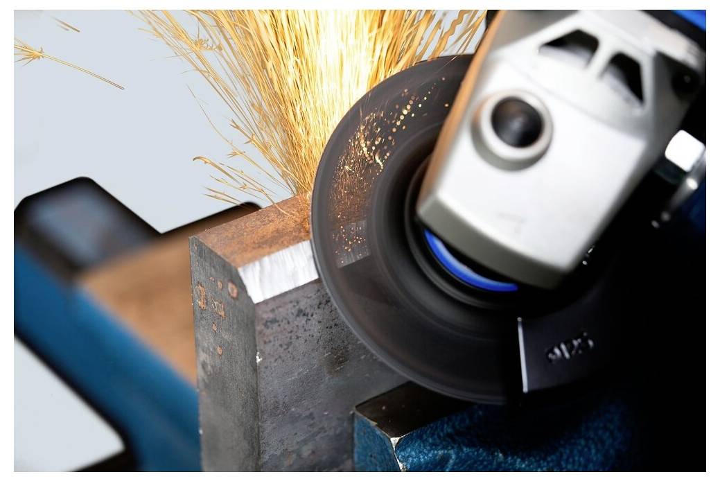 Et nærbillede af en metalslibemaskine i aktion, der slifer en metalblok med gnister, der flyver rundt, hvilket viser industrielt arbejde og værktøjspræcision.