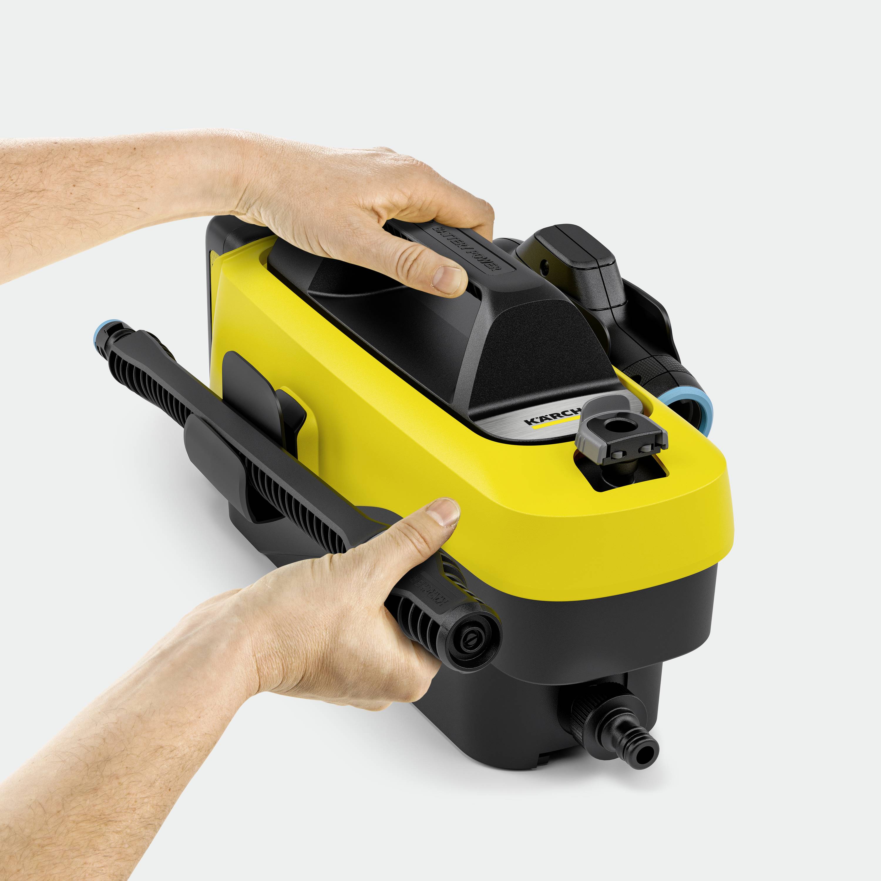 To hænder holder en gul højtryksrenser med sort håndtag, egnet til udendørs rengøringsopgaver.