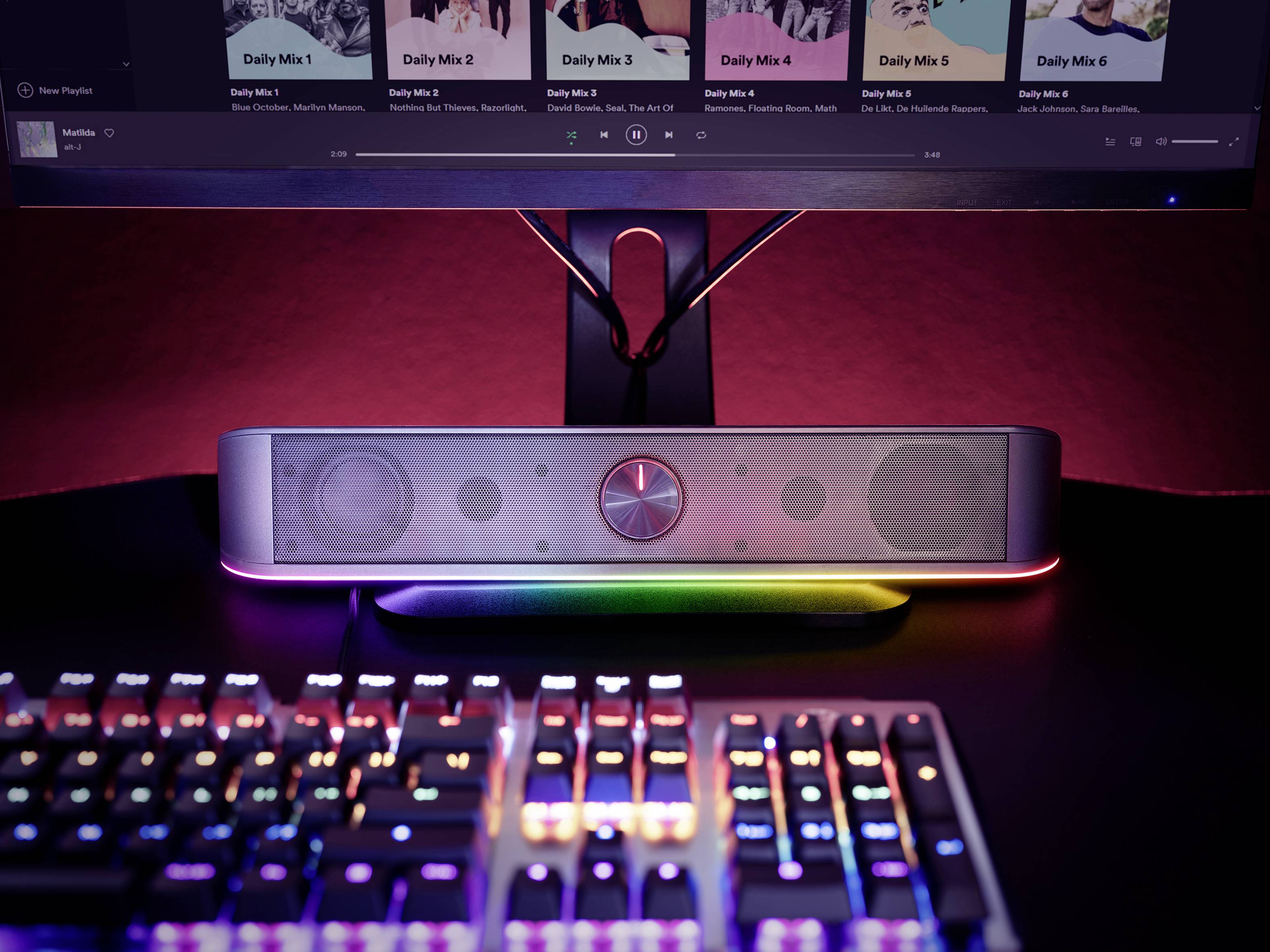 Arbejdsplads med belyst tastatur, højttalere og skærm. På skærmen ses en musikafspiller med playlister.