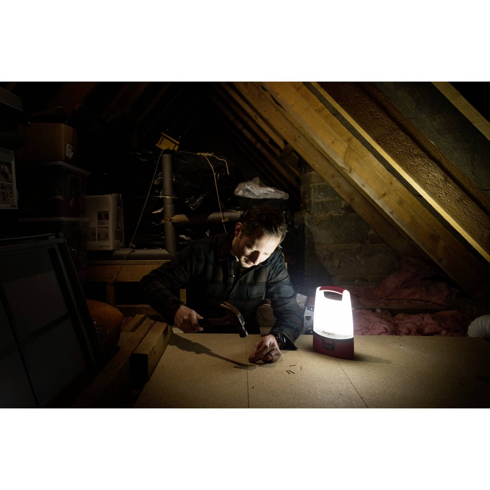 En mand arbejder med en hammer på et loft, belyst af en lampe. Han er fokuseret på projektet foran sig.