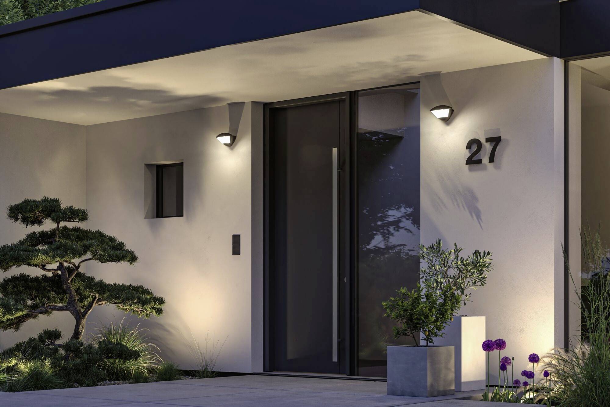 Moderne hoveddør til et hus om natten, belyst af udendørslamper. Husnummer 27 er synligt. Dekorative planter foran.
