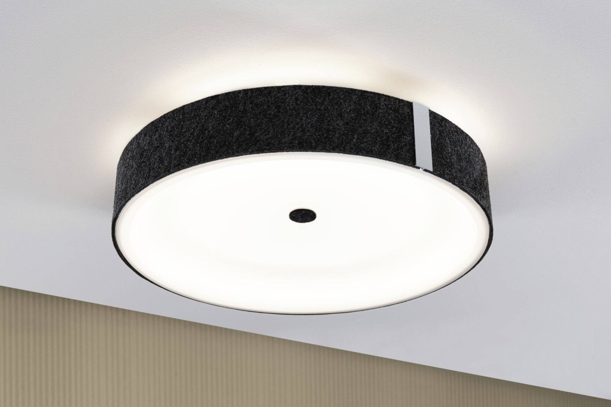 Enkel, rund loftslampe med sort ramme og centralt placeret kontakt, monteret på den hvide loft i et moderne rum.