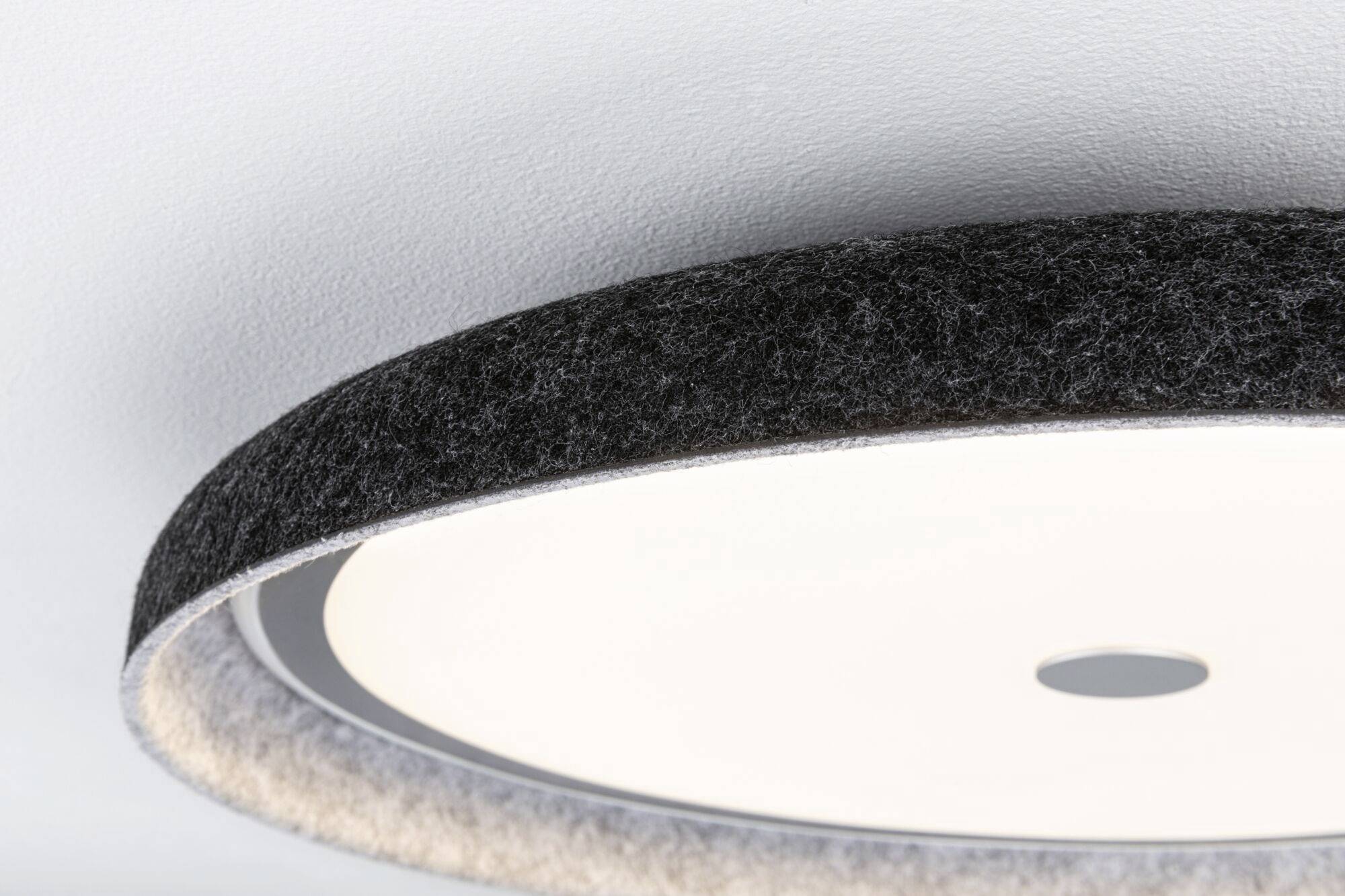 Nærbillede af en rund loftslampe med en sort filtkantet, der udsender et blødt, diffust lys.