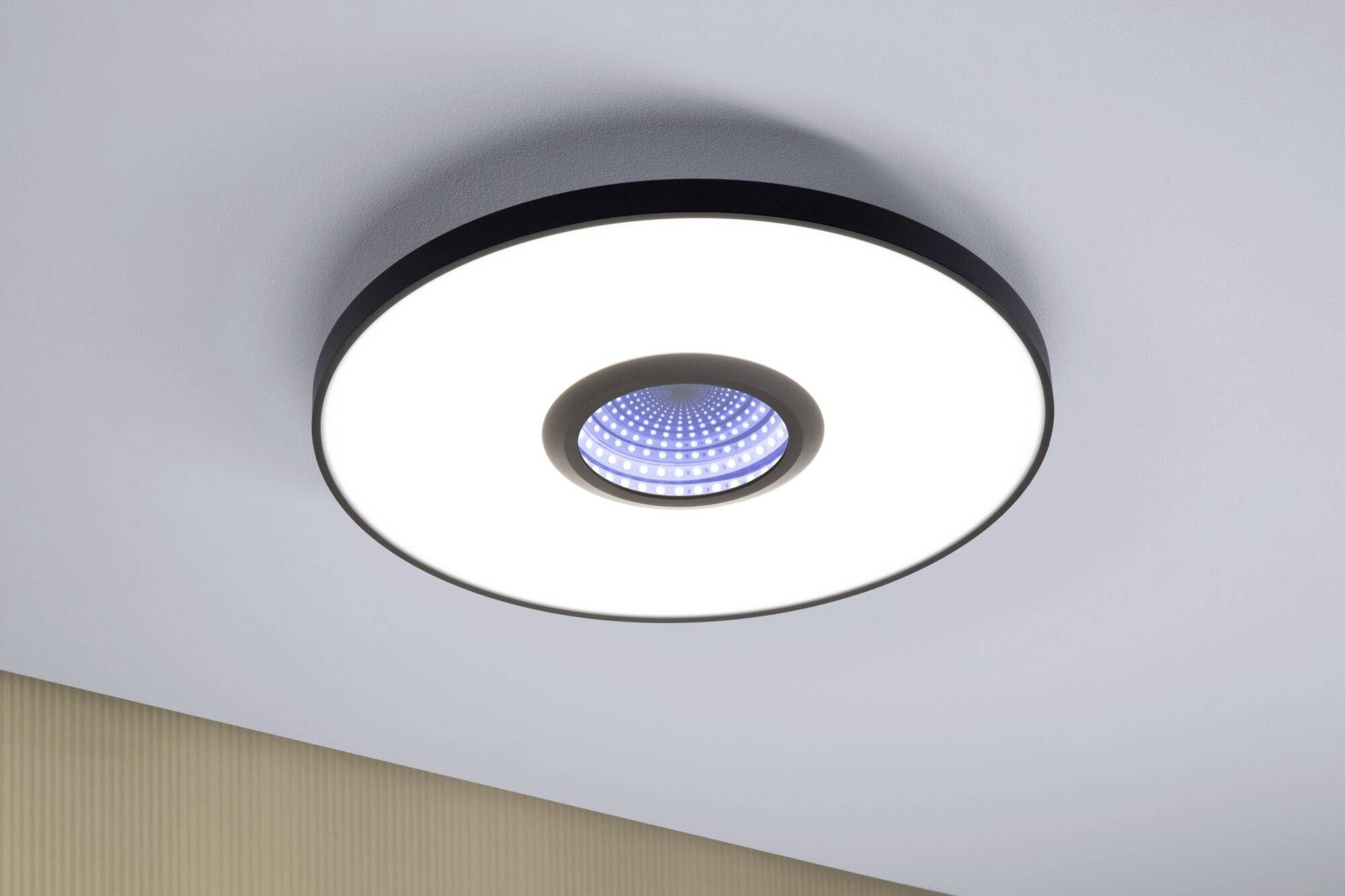 En rund loftslampe med et centralt blåt LED-element, monteret på en hvid loft, afgiver et klart lys.