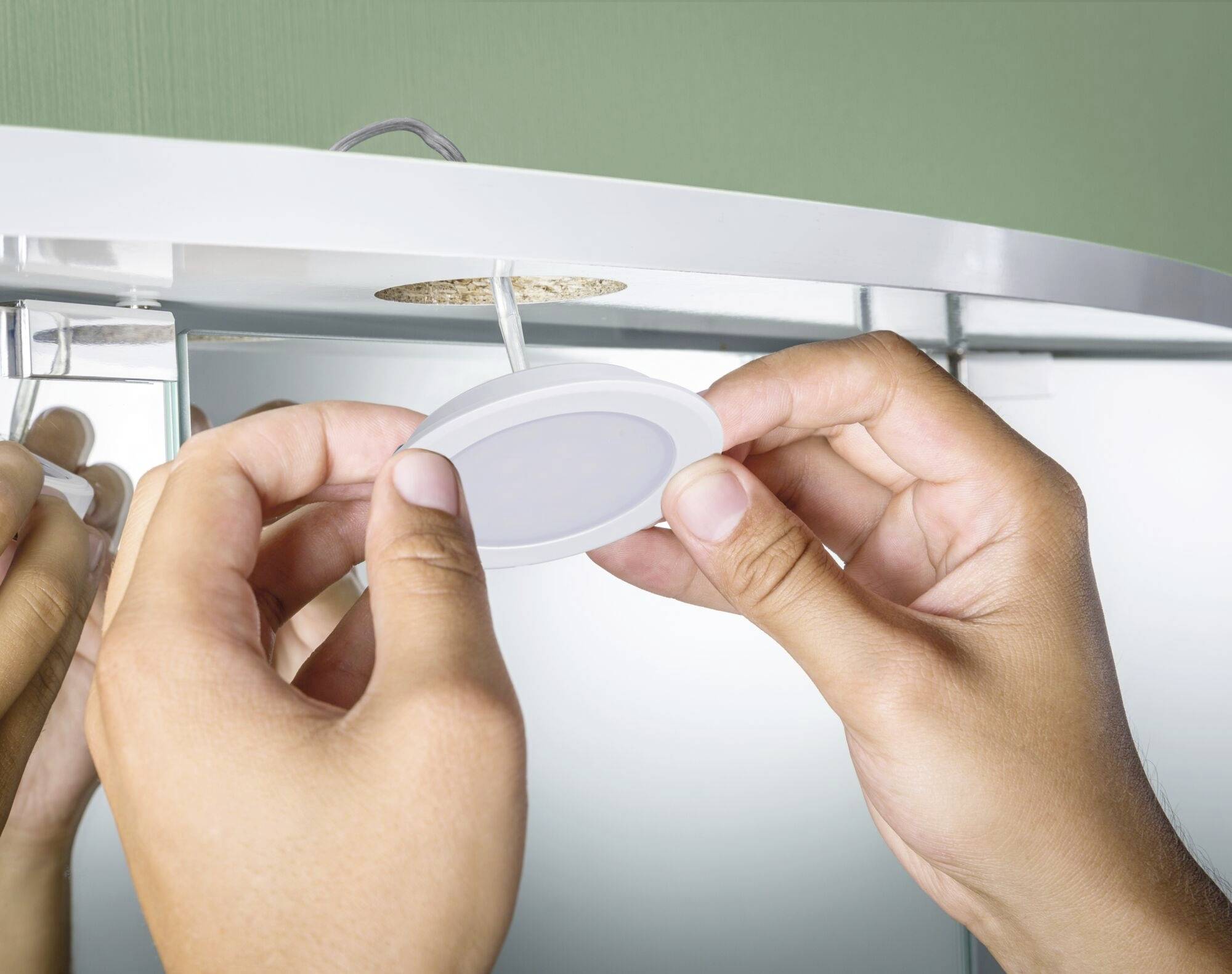 En person installerer et rundt LED-panel i loftet i et rum. Hænder holder lyset og fører det ind i en åbning.