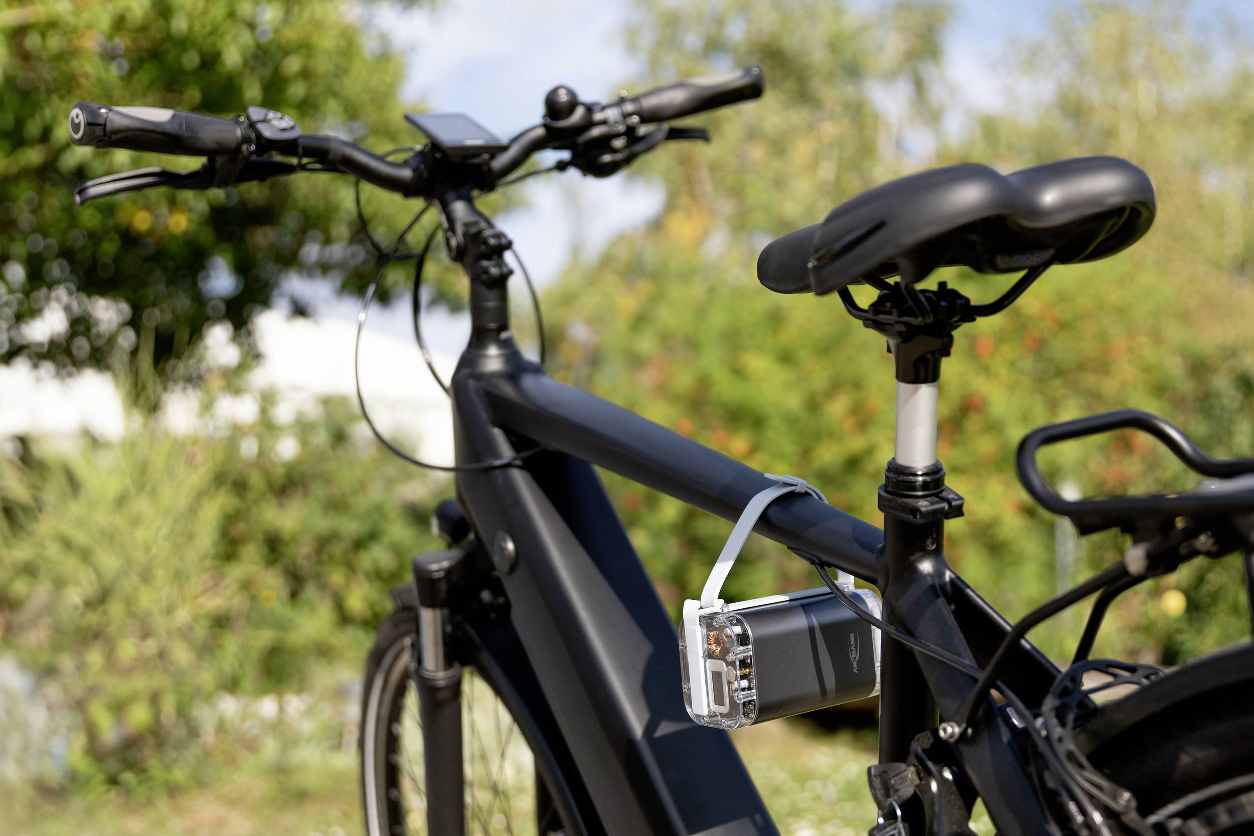 El-cykel med fastgjort GPS-enhed på rammen. I baggrunden træer og en skyet himmel. Fokus på cyklens teknologi.
