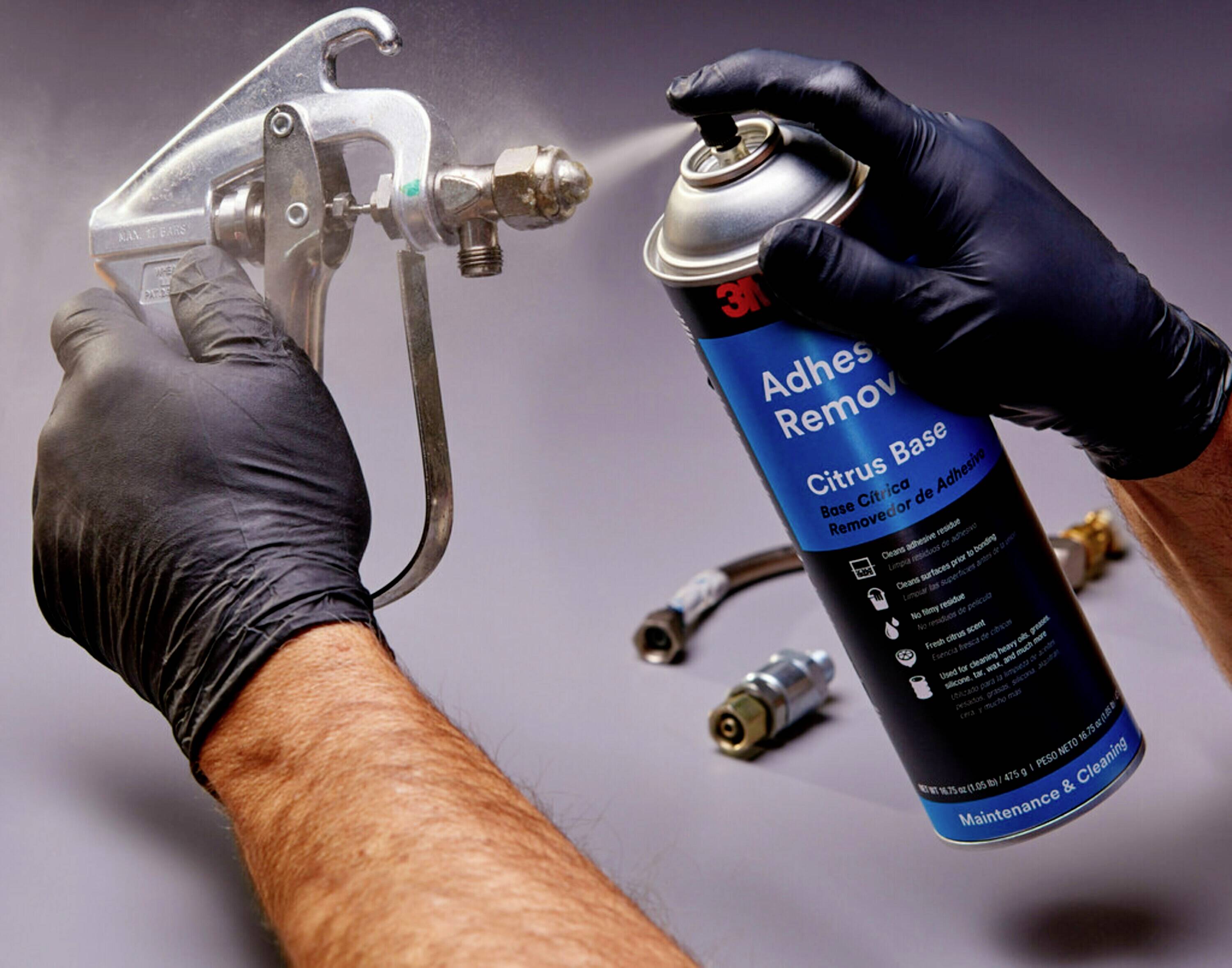 En person med sorte handsker sprayer fra en spraydåse 'Adhesive Remover'. Dåsen er blå med et citrus-baseret etiket.
